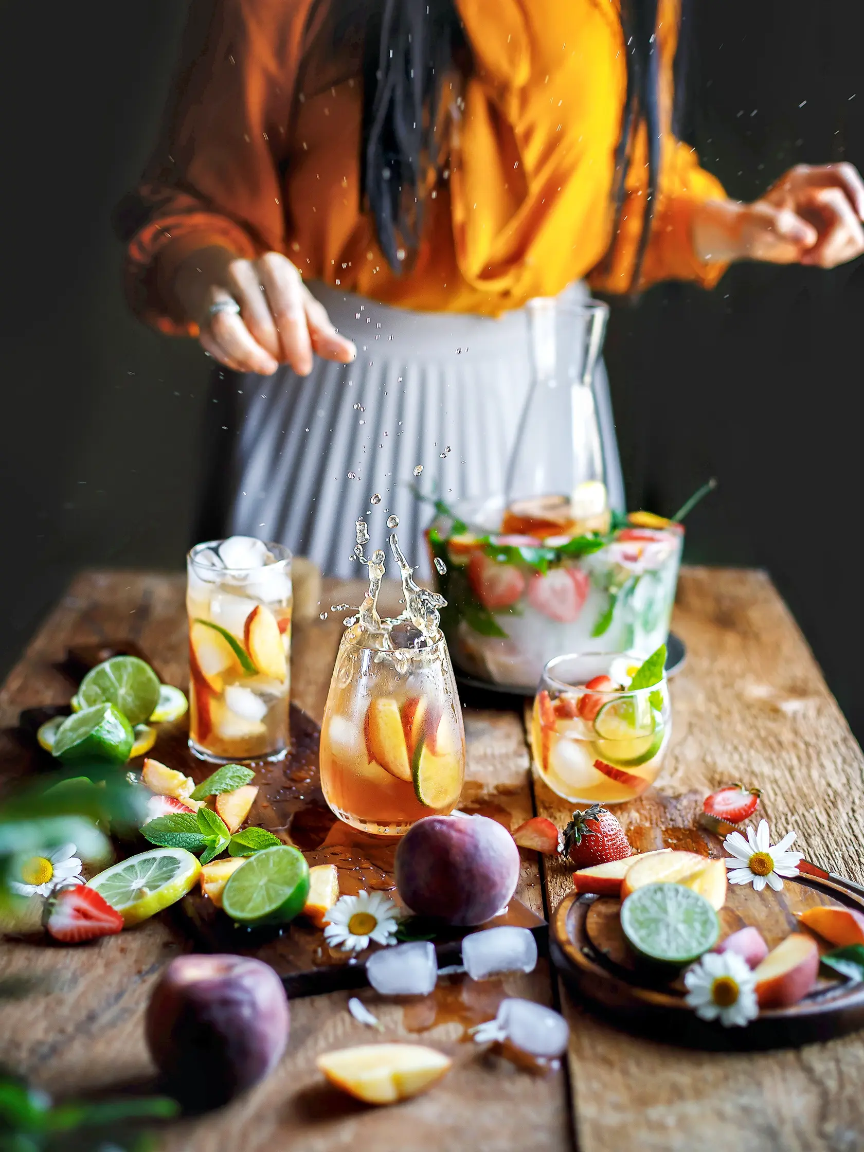 Peach lemonade with strawberries, limes, summer lemonade with ice on the black dark rustic background. Women pours lemonade to the glass, splash of lemonade