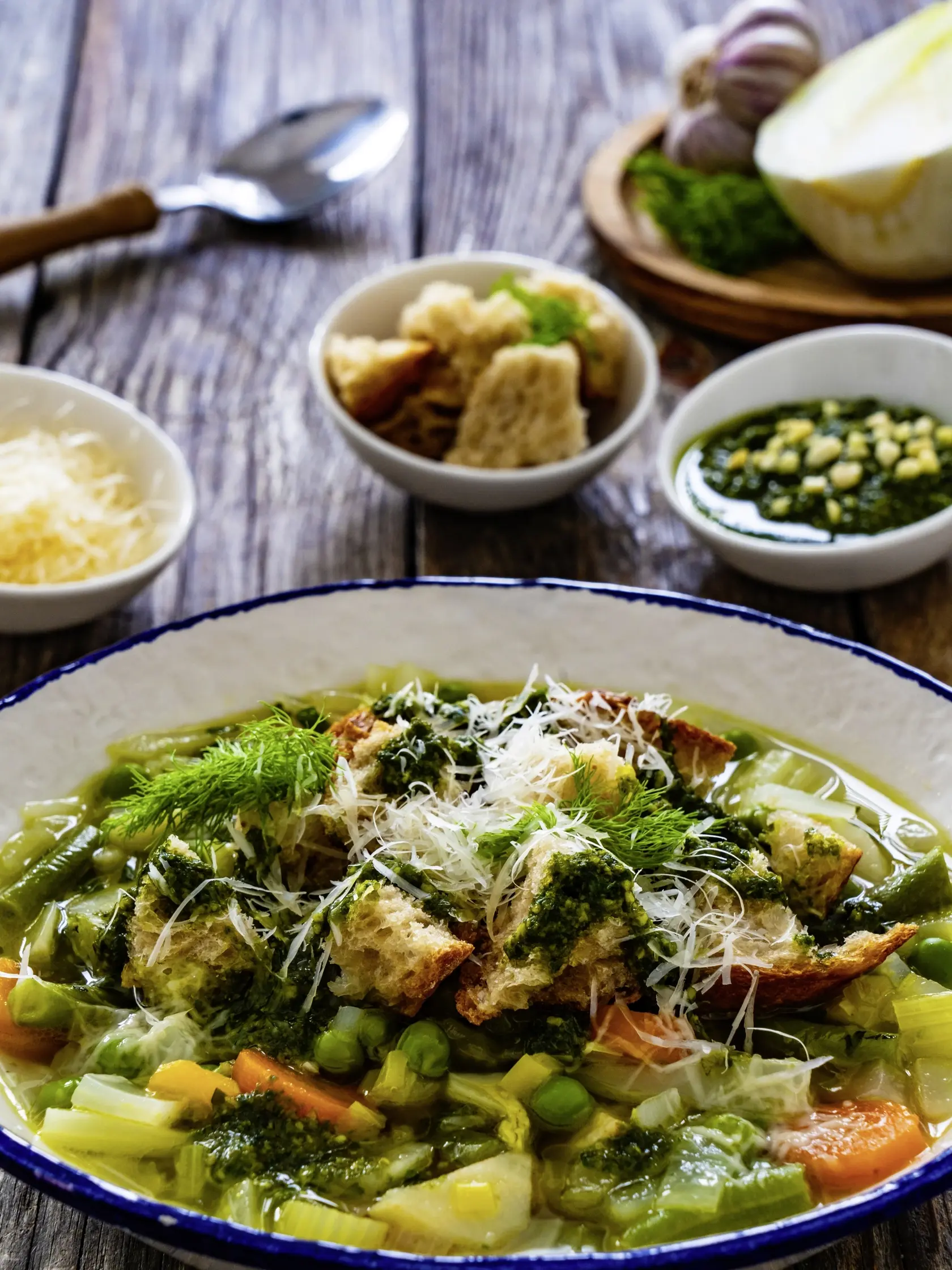 Pistou soup Nice - broth with basil pesto, bread, cheese and vegetables on wooden background in white bowl 
