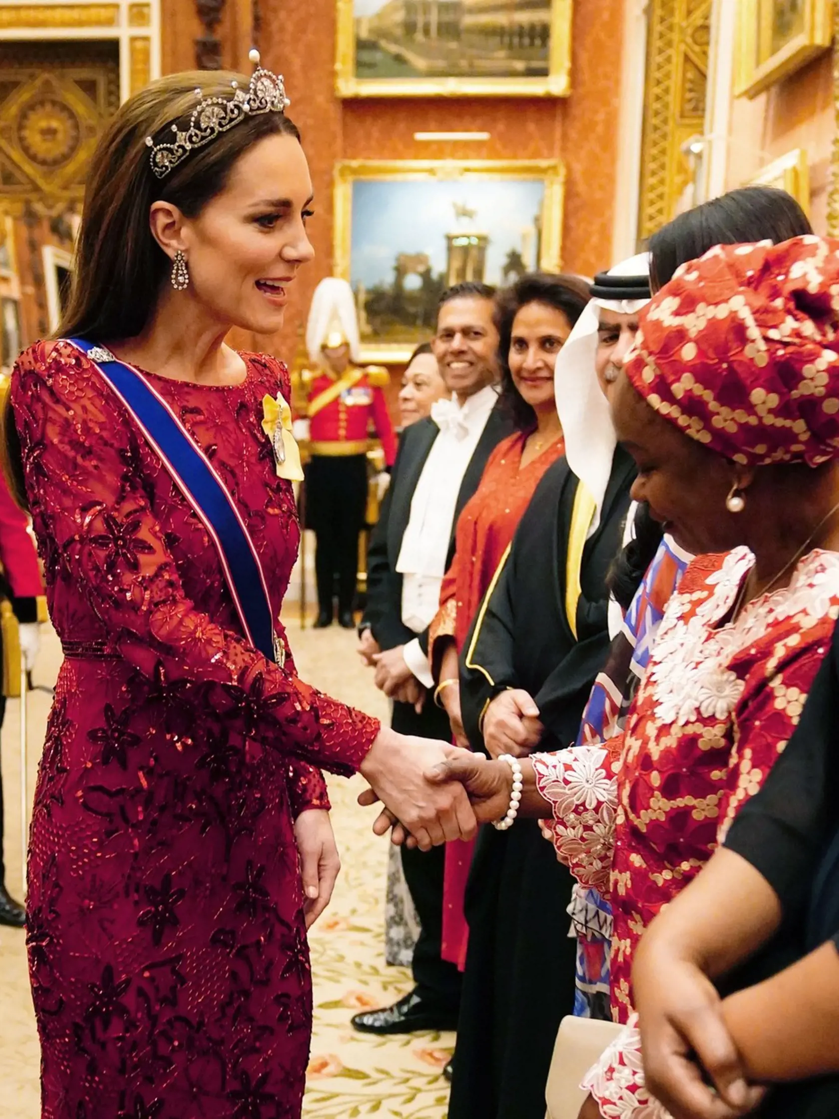 Princezná Kate ako vždy neuveriteľne zažiarila. Vlasy si opäť nechala vyzdobiť úžasným doplnkom z kráľovského trezoru. Diadém s červenou róbou, ako aj s modrou vlečkou a jej žltým kráľovským rodinným rádom.