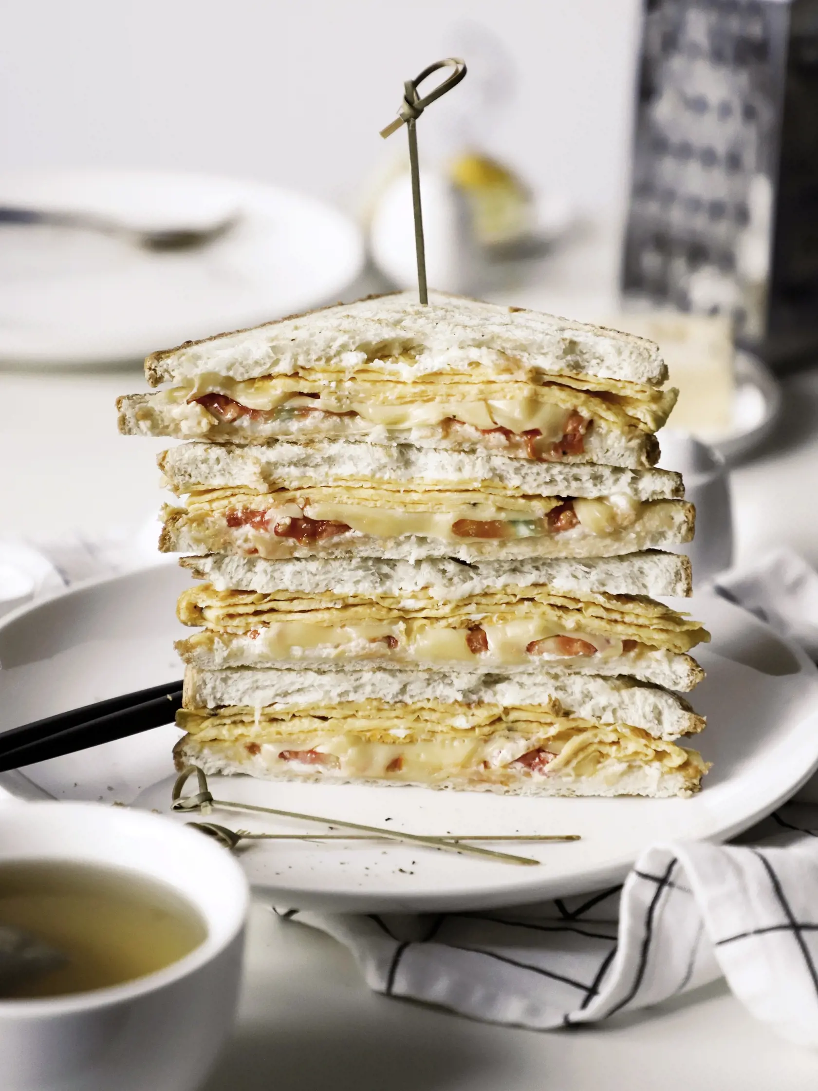 tower of triangular sandwiches with cheese, tomatoes and egg omelette in section on the plate, ingredients on the breakfast table, healthy vegetarian food, white background, close up