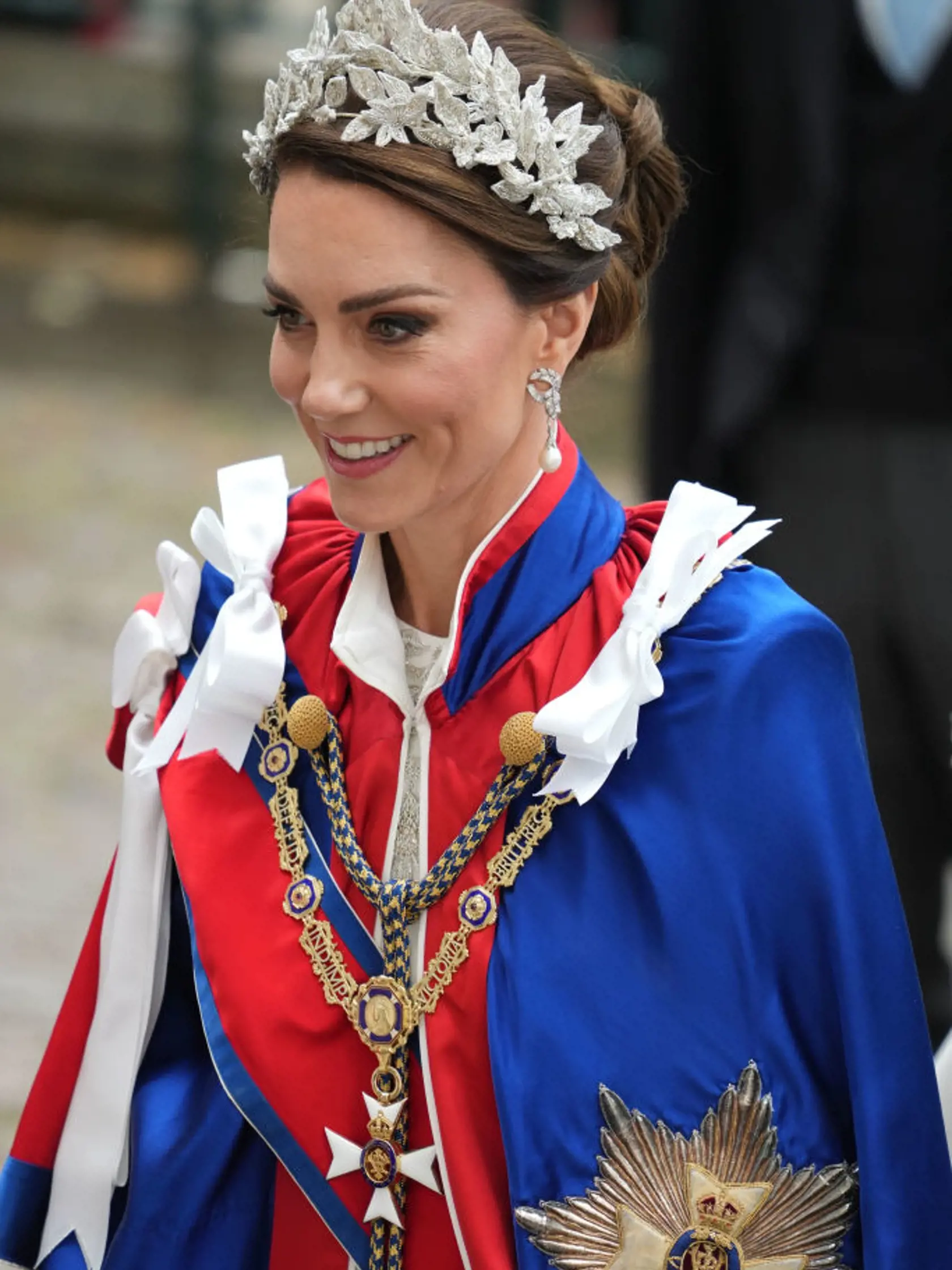Princezná Kate mala na sebe tradičný ceremoniálny plášť. Pod ním slonovinové šaty od Alexandra McQueena a 3D čelenku, rovnako tak aj jej dcéra, princezná Charlotte.