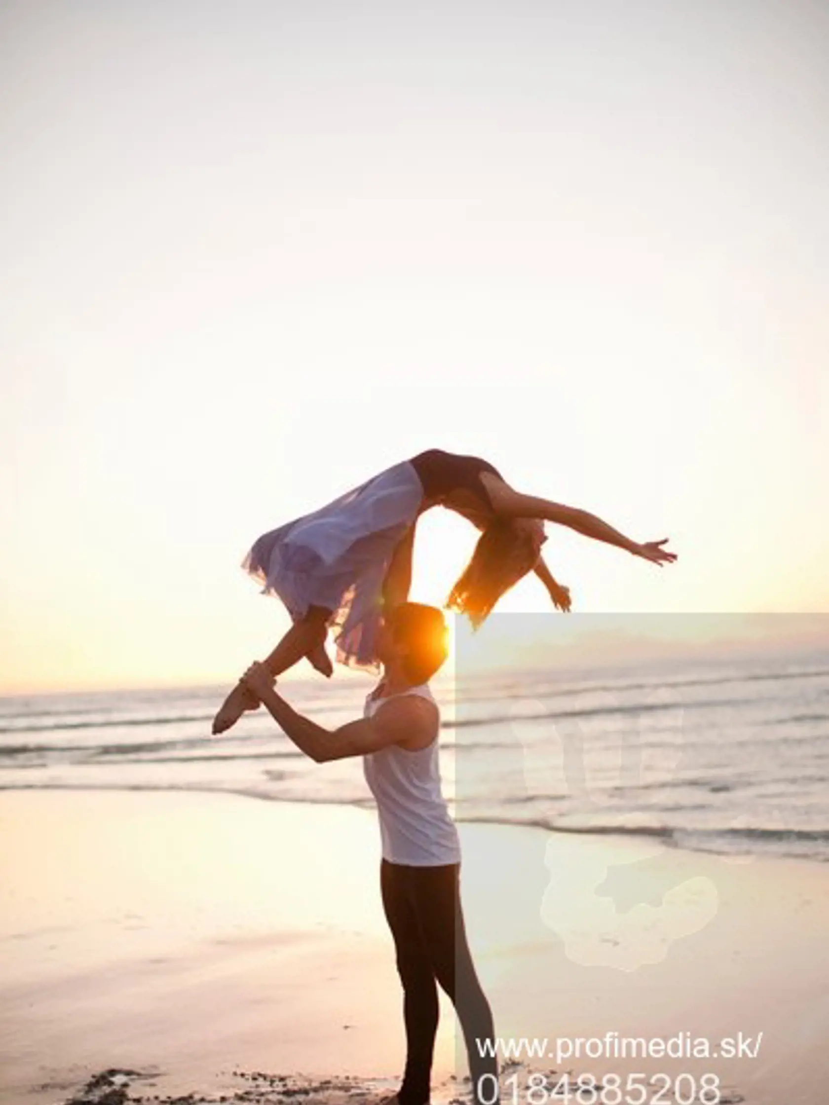 Young man lifting dancing partner on sunlit beach