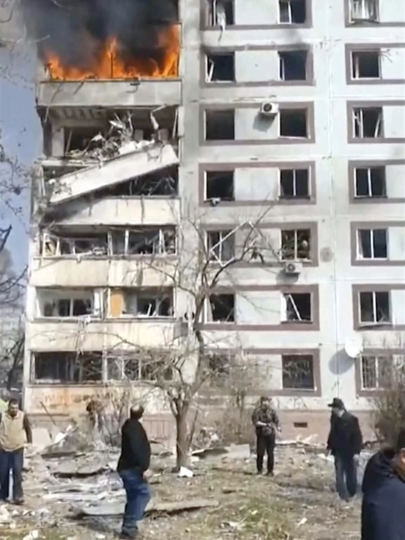 Na videosnímke, ktorú poskytla kancelária ukrajinského prezidenta, ľudia stoja pred horiacou výškovou obytnou budovou, ktorú zasiahlo ostreľovanie v meste Záporožie na juhovýchode Ukrajiny v stredu 22. marca 2023.