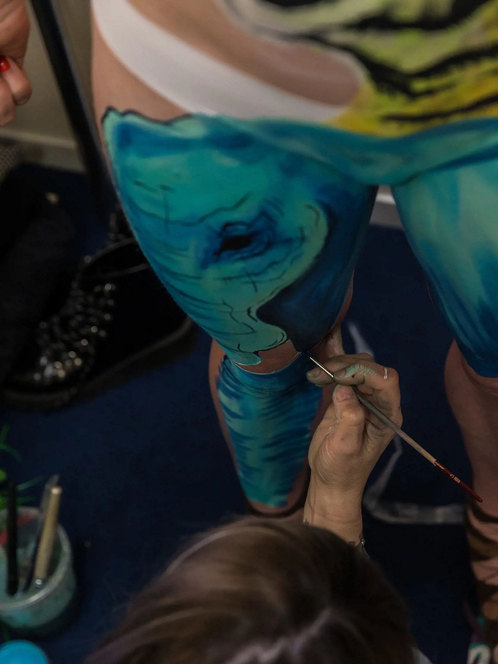 Bodypainter na Interbeauty v Inchebe maľuje detaily na stehno modelky.