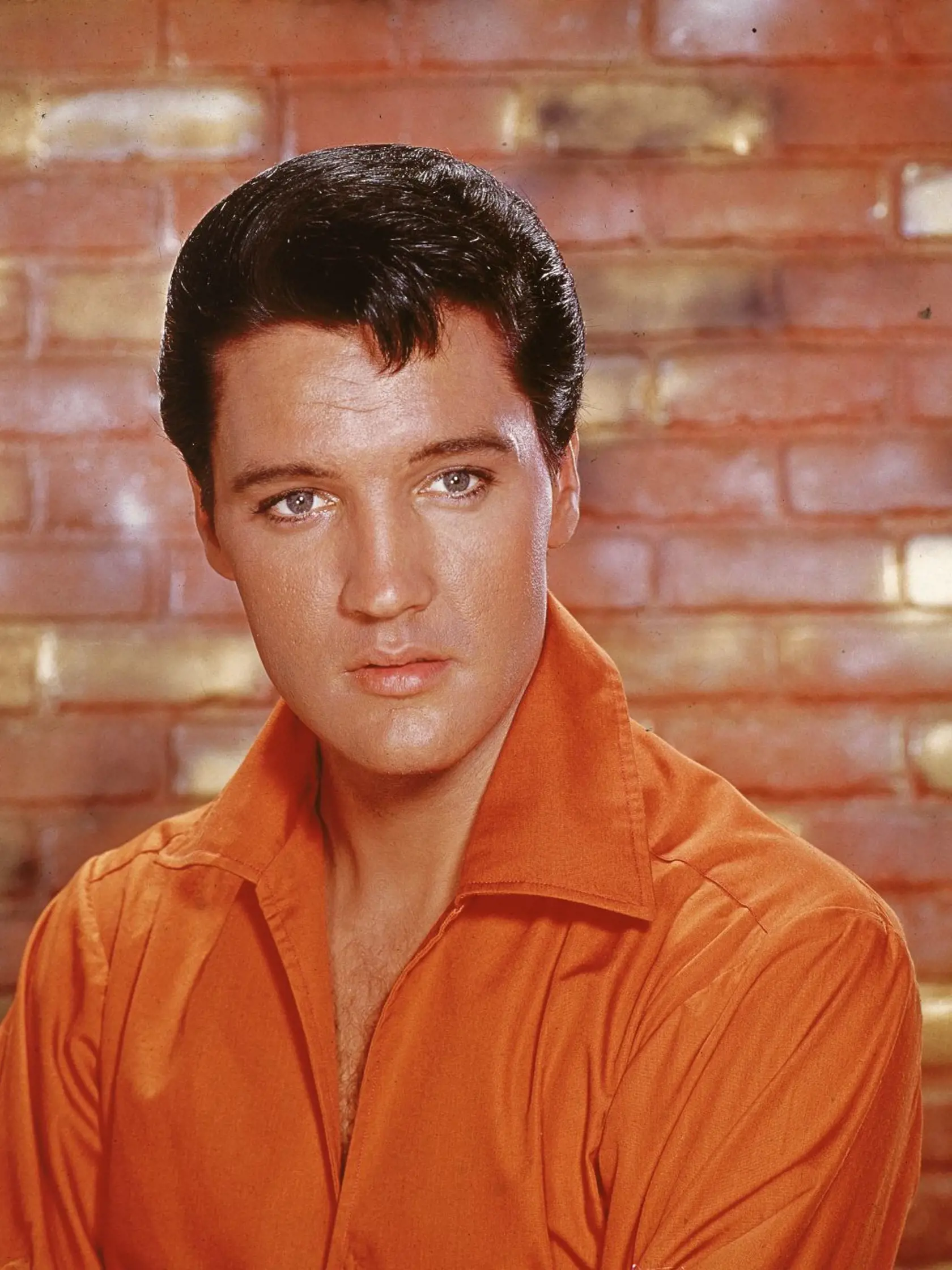 Portrait of American rock and roll singer Elvis Presley, dressed in an orange open-neck shirt and in front of a brick wall, mid 1960s. (Photo by Hulton Archive/Getty Images)