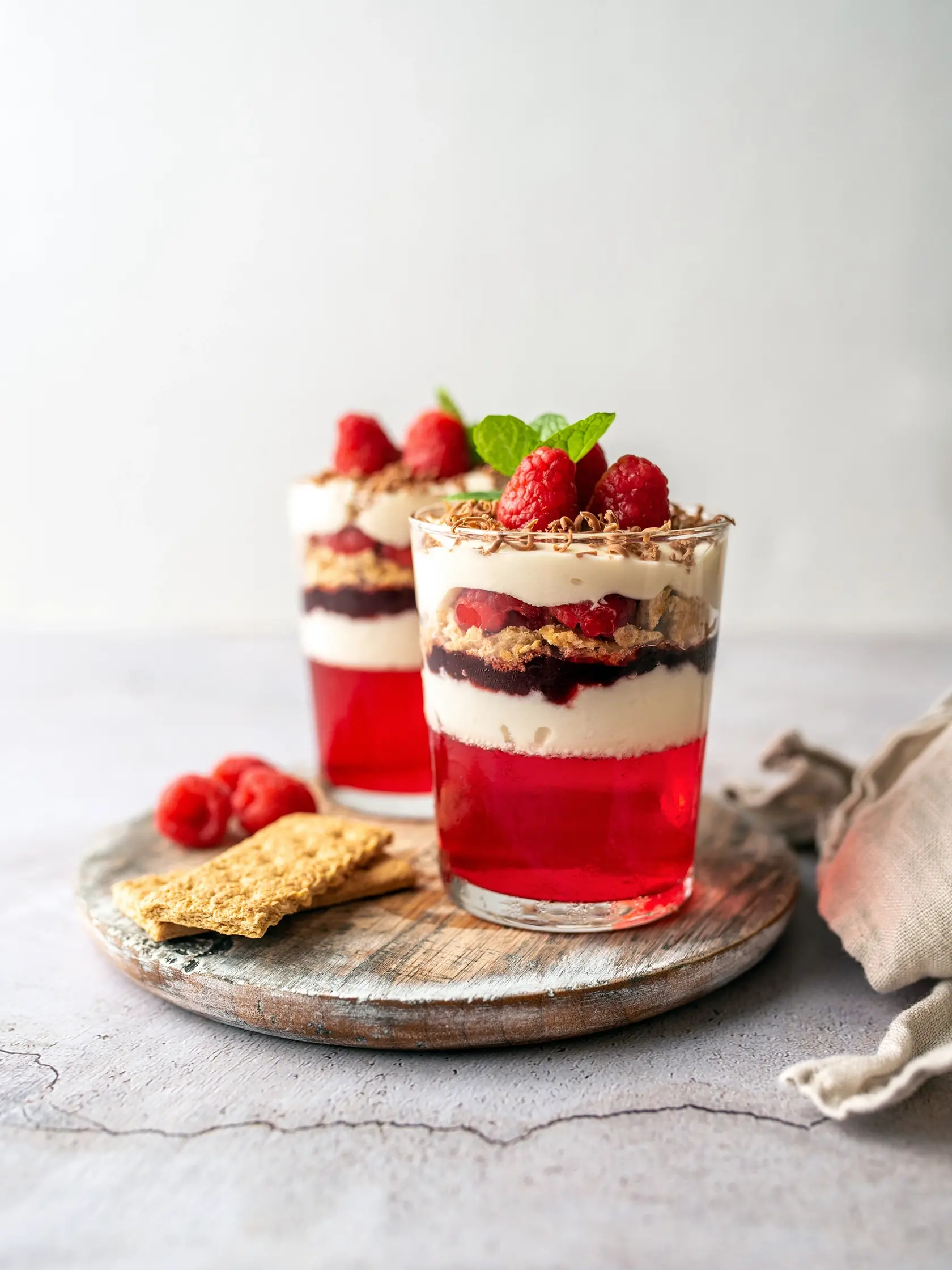 Dessert in a glass cup, with Jello covered in yogurt and topped with fresh raspberries. Mini dessert on light concrete background. Fruit parfait with jello and jelly.