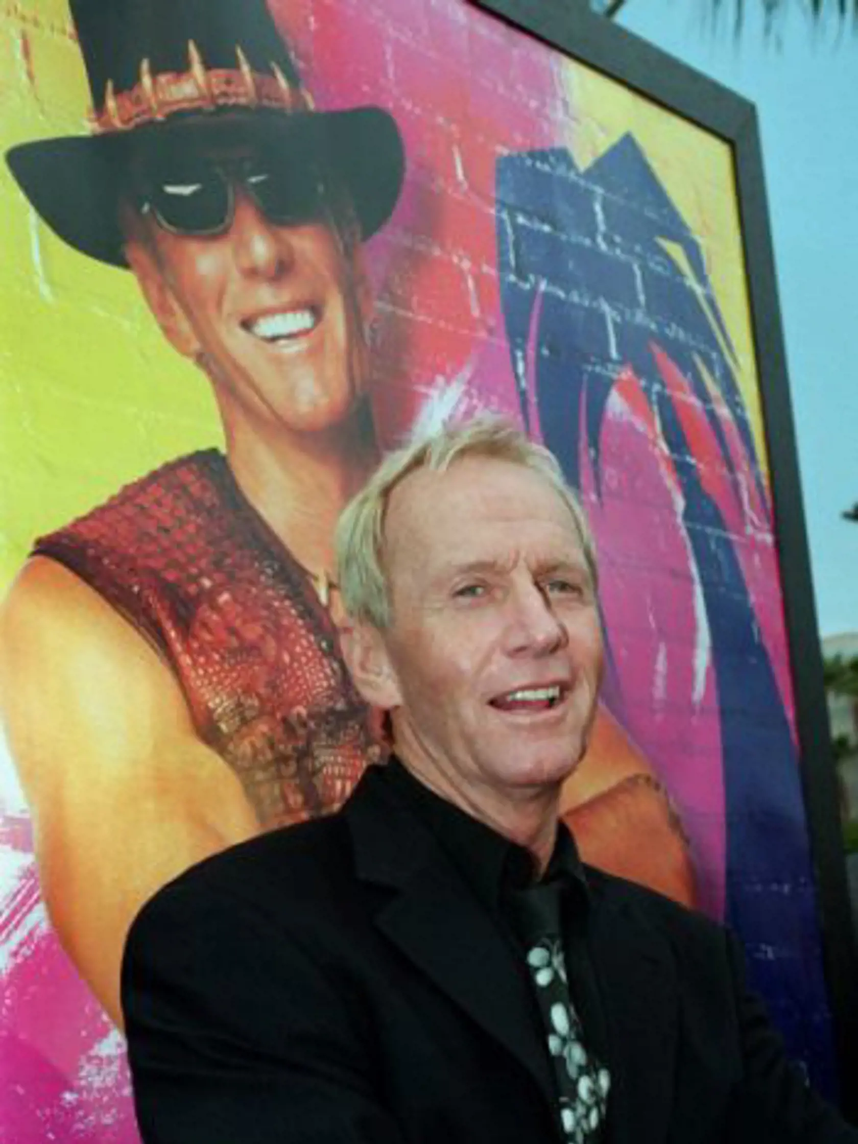 ** FILE ** In this April 18, 2001 file photo, Australian actor Paul Hogan, star of the "Crocodile Dundee" movie trilogy poses in front of a movie poster for "Crocodile Dundee in Los Angeles," at a screening of the movie, at the Paramount studios in Los Angeles. Hogan, has been barred from leaving Australia until he pays a multimillion dollar tax bill his lawyer said on Thursday, Aug 26, 2010.(AP Photo/Rene Macura, File)