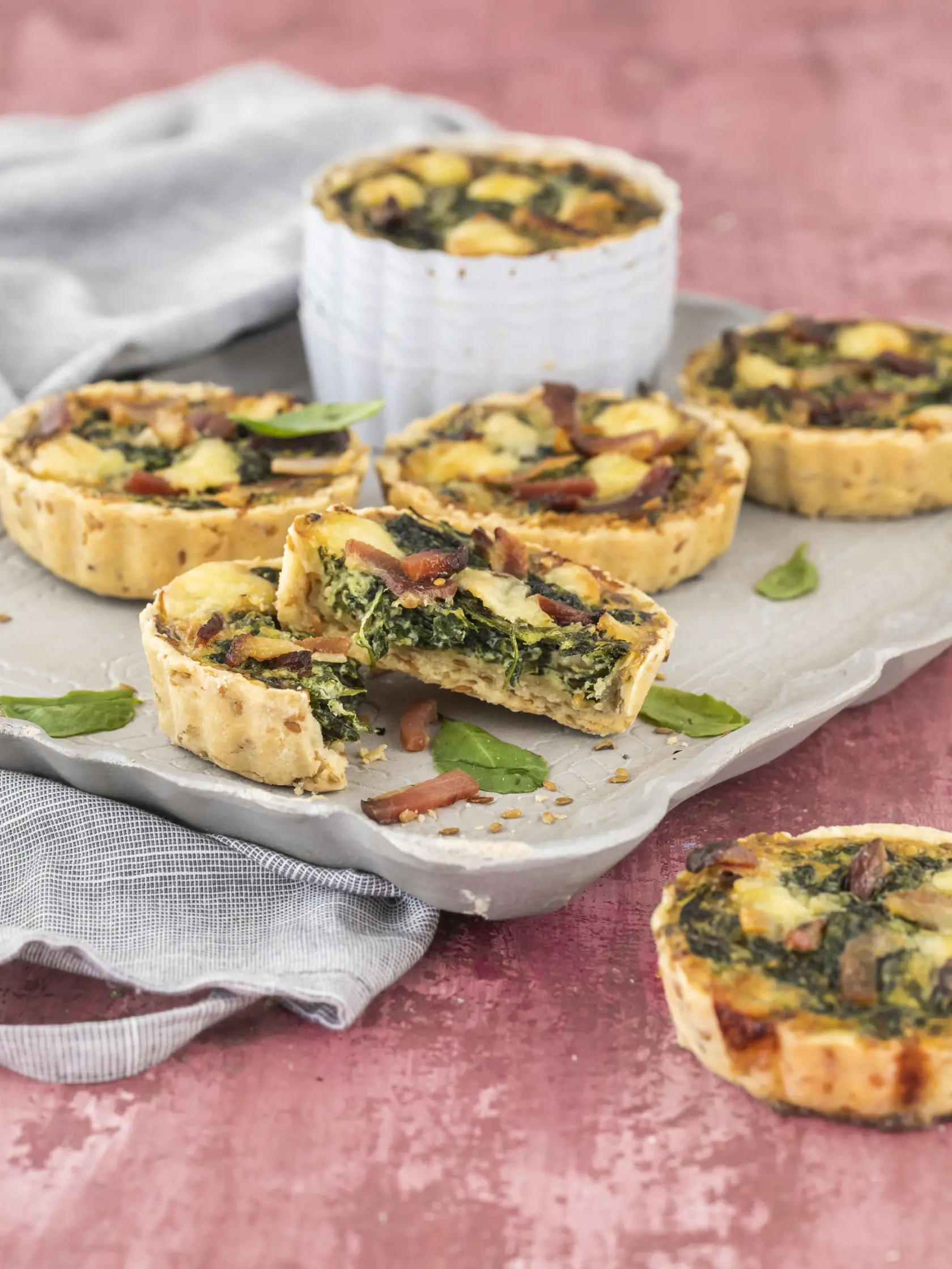 špenátovo slaninové minikiše

recept:
6 KUSOV, PRÍPRAVA 30 MINÚT,
PEČENIE 35-40 MINÚT
NA CESTO:
• 175g hladkej špaldovej múky
• 30g sezamových semiačok
• 100g masla
• pol lyžičky soli
• 1 žĺtok
• 3-4 lyžice studenej vody
(ak treba)
NA NÁPLŇ:
• 1 lyžica olivového oleja
• 1 strúčik cesnaku
• 1 hrnček sparených
špenátových listov
• 3 vajcia
• 3 plátky slaniny
(nakrájanej na prúžky)
• 100g čedaru
• 200ml smotany na šľahanie
• 50g kyslej smotany
(alebo hustého jogurtu)
• štipka mletého muškátového
or