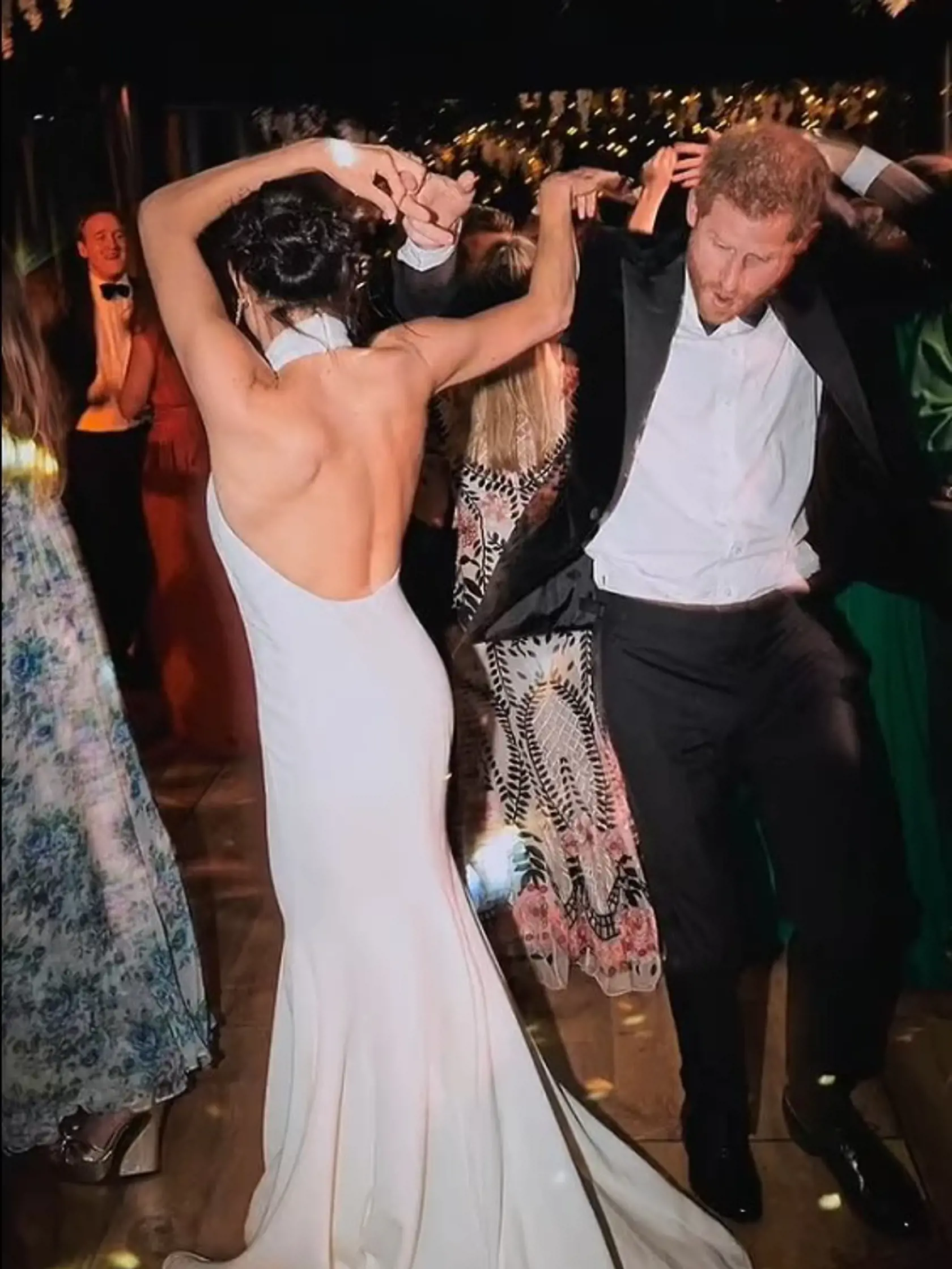 Namiesto honosných šiat má Meghan na záberoch jednoduché biele dlhé šaty s odhalenými ramenami a hlbokým výstrihom na chrbte.