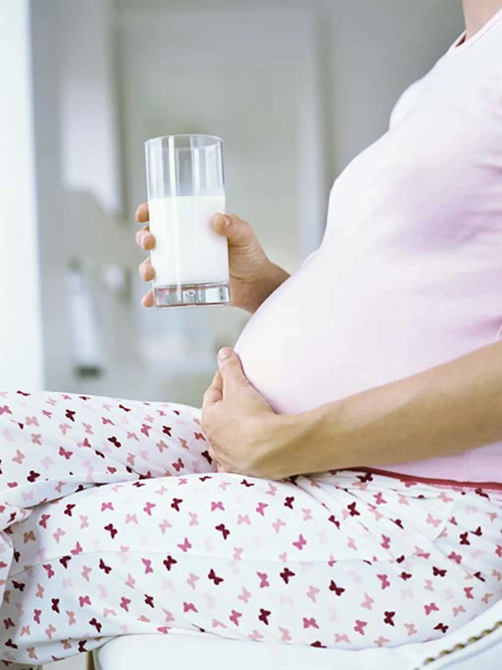mid section view of a pregnant woman holding a glass of milk and touching her abdomen