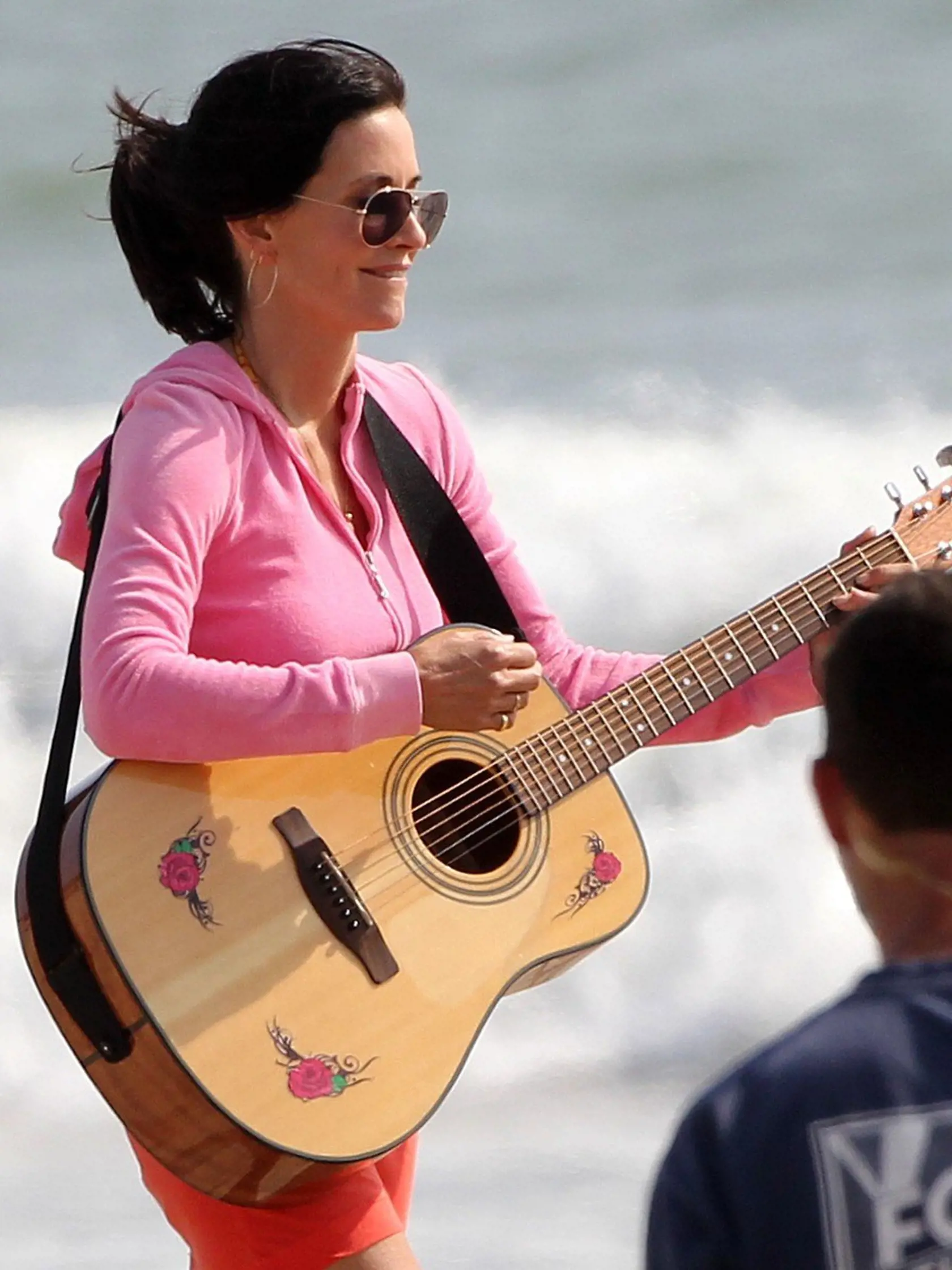 38952, LOS ANGELES, CALIFORNIA - Thursday March 25, 2010. Courtney Cox and the cast of Cougar Town spend  a relaxing day at the beach in Los Angeles, filming an upcoming episode. Courtney is seen riding a bike wearing an orange dress and a pink zip up sweater and later playing football won the beach. Co-stars Busy Philipps, Dan Byrd, Ian Gomez, and Brian Van Holt are also seen on the beach, drinking in red plastic cups and what looks like wine bottles. Brian Van Holt's character is seen being bu