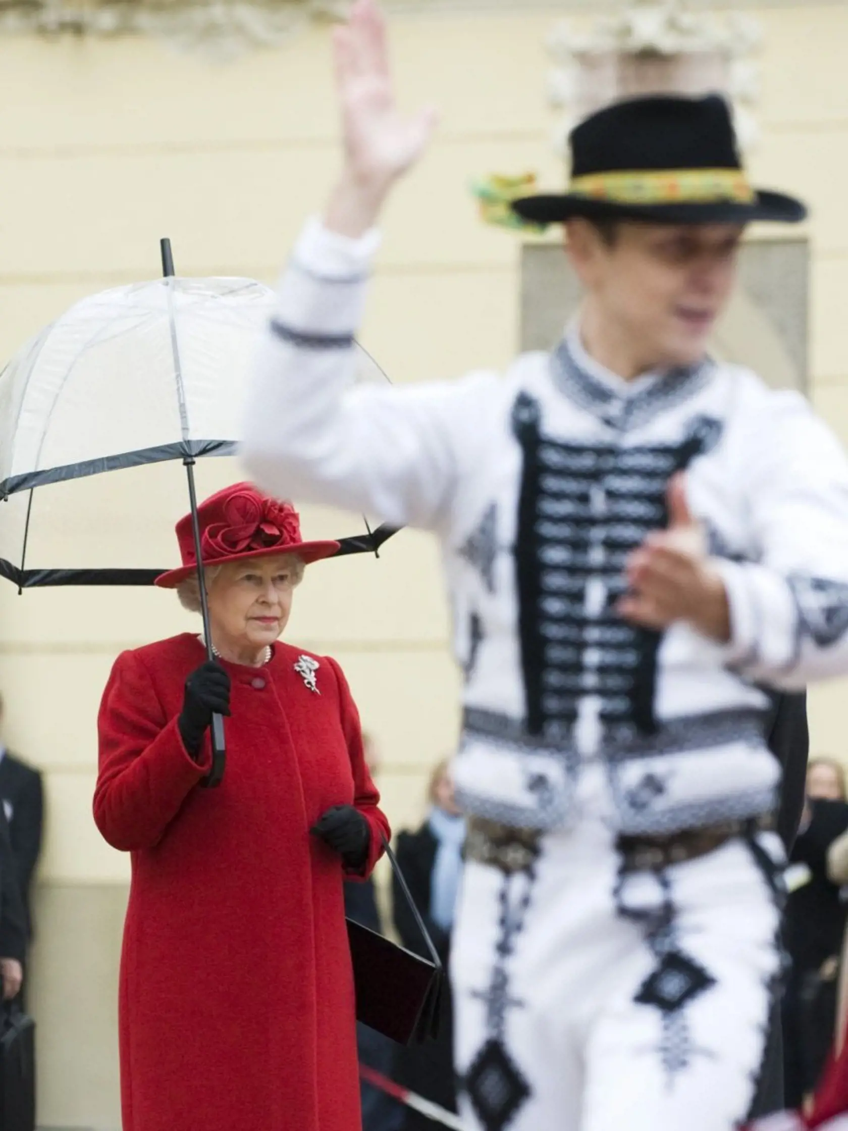 Neobvyklý záber: Alžbeta II. pod dáždnikom sleduje folklórny tanec.