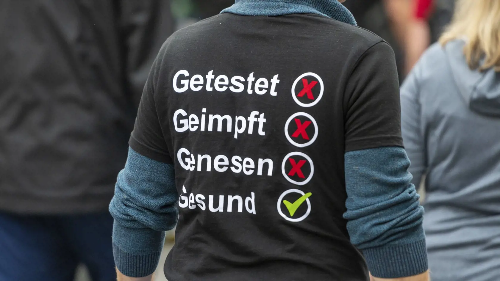 Muž má tričko s nápisom testovaný, očkovaný, prekonal ochorenie COVID-19, zdravý počas ďalšieho protestu odporcov protipandemických opatrení v Berlíne.