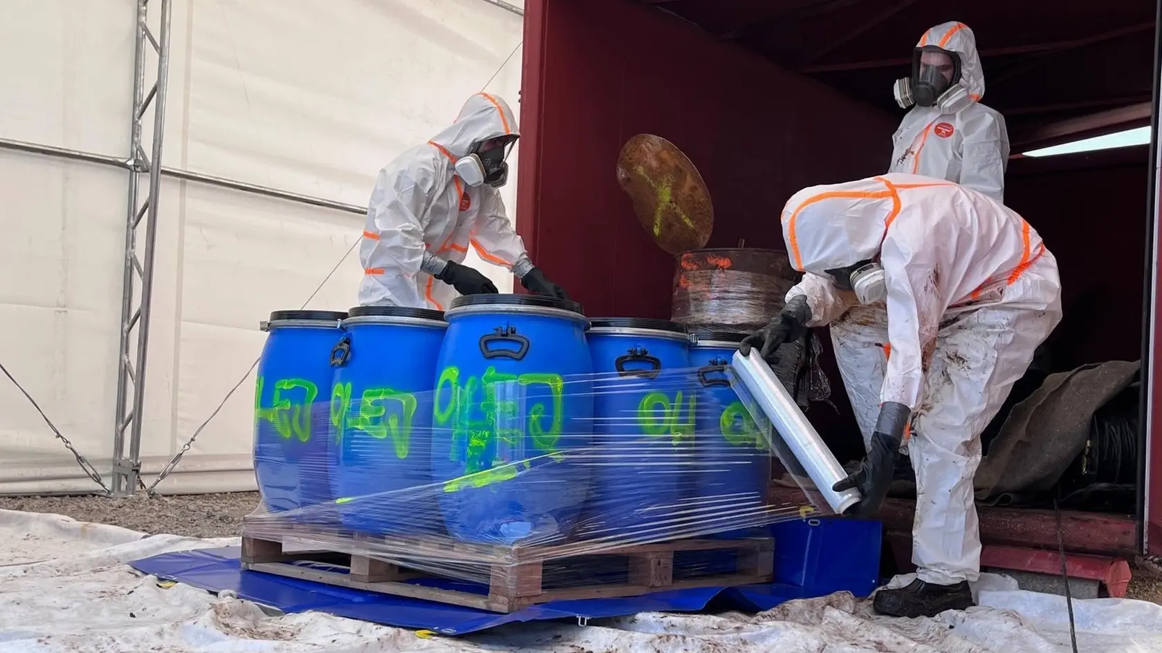 Chemikálie odvážajú pracovníci v špeciálnych oblekoch.
