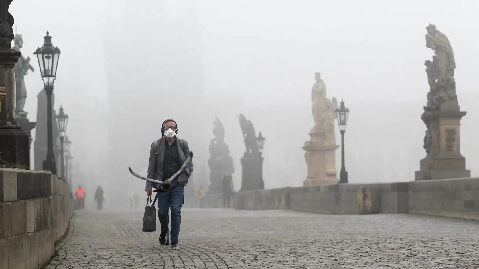 WA 34 Praha - Muž s respirátorom kráča po Karlovom moste počas hmlistého rána v Prahe v stredu 24. februára 2021. Česká republika pristúpila na ďalšie sprísňovanie epidemiologických opatrení v boji proti nákazlivejším variantom nového typu koronavírusu. V rámci členských krajín EÚ patrí Česko k jedným z najviac postihnutých krajín nákazou. Zhoršujúca epidemiologická situácia prinútila český kabinet  odložiť otvorenie všetkých obchodov. FOTO TASR/AP

A man wears a face mask as he walks across the