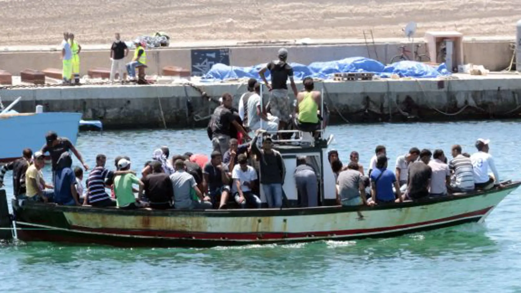 Loï s africkými imigrantmi sa plaví cez prístav na talianskom ostrove Lampedusa 1. augusta 2011, kde v pozadí vidie màtve telá a truhly 25 Afrièanov, ktorí utekali z Líbye. Dvadsapä màtvych tiel našli v pondelok v nákladnom priestore preplnenej lode zo severnej Afriky pri talianskom ostrove Lampedusa. Na približne 15 metrov dlhej lodi sa nachádzalo spolu takmer 300 migrantov, medzi nimi 36 žien a 21 detí.