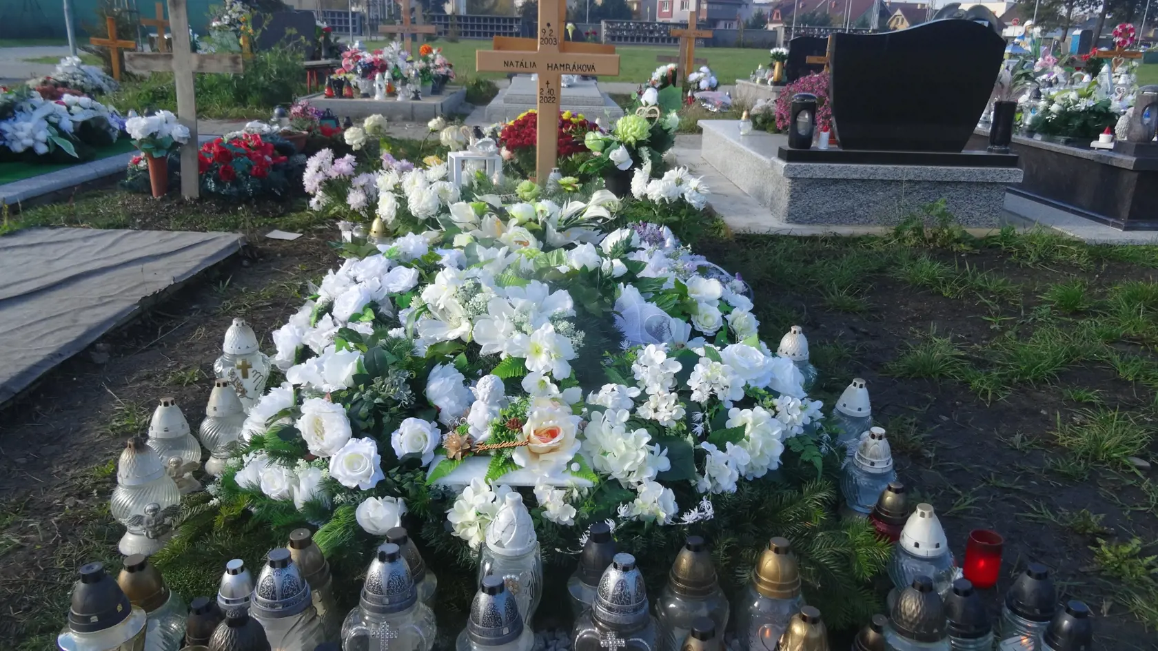 Hrob Natálie obsypaný kvetmi a vencami. Vpredu na podložke horelo množstvo kahancov.