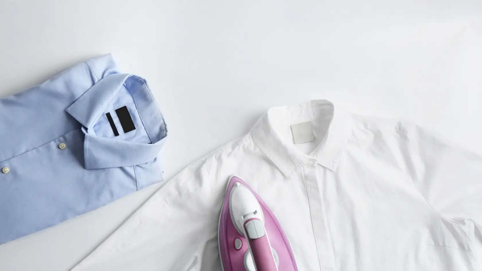 Iron with clean shirts on light background, top view