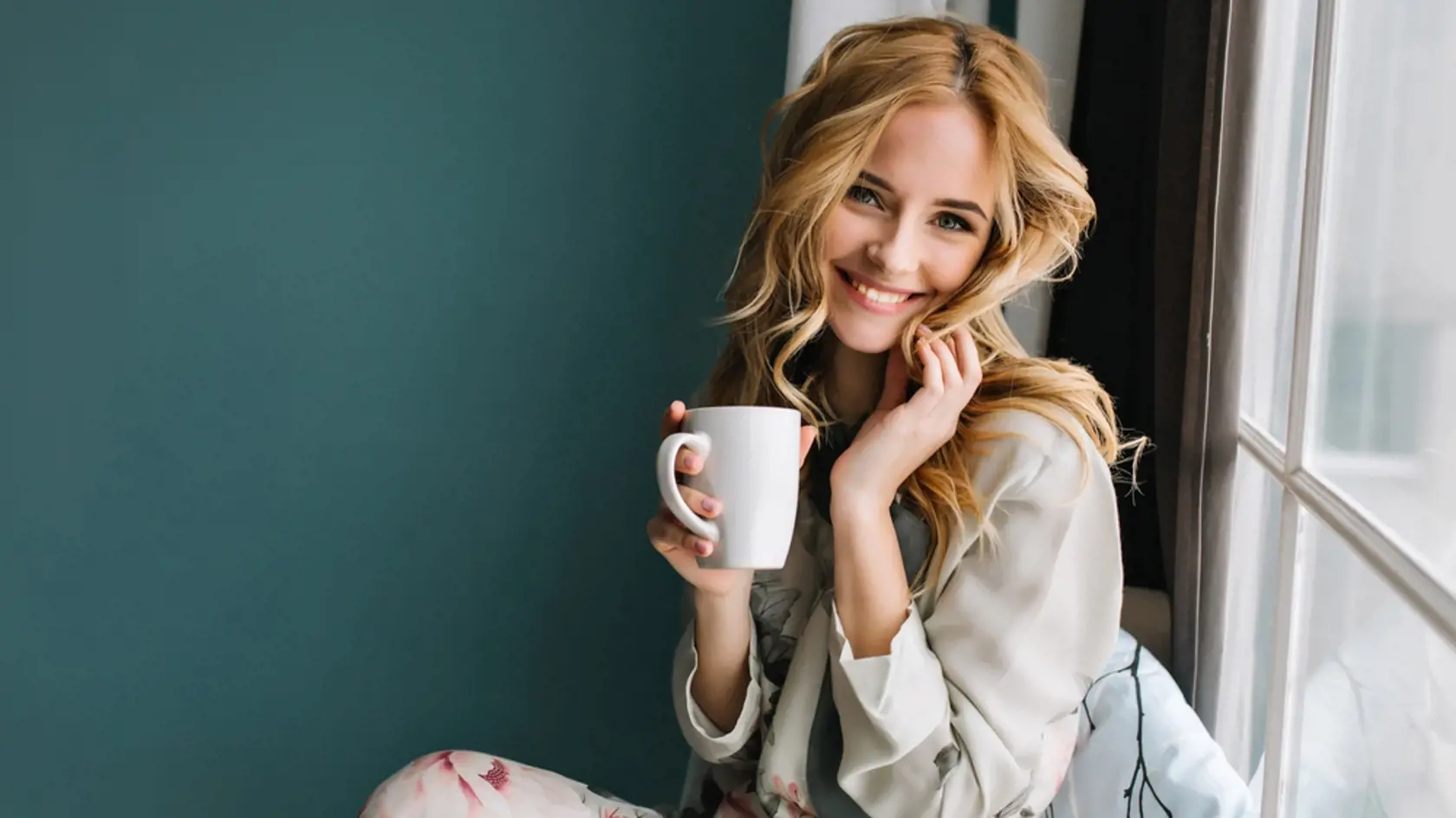 Cheerful,Blonde,Woman,Relaxing,And,Sitting,On,Window,Sill,,Holding