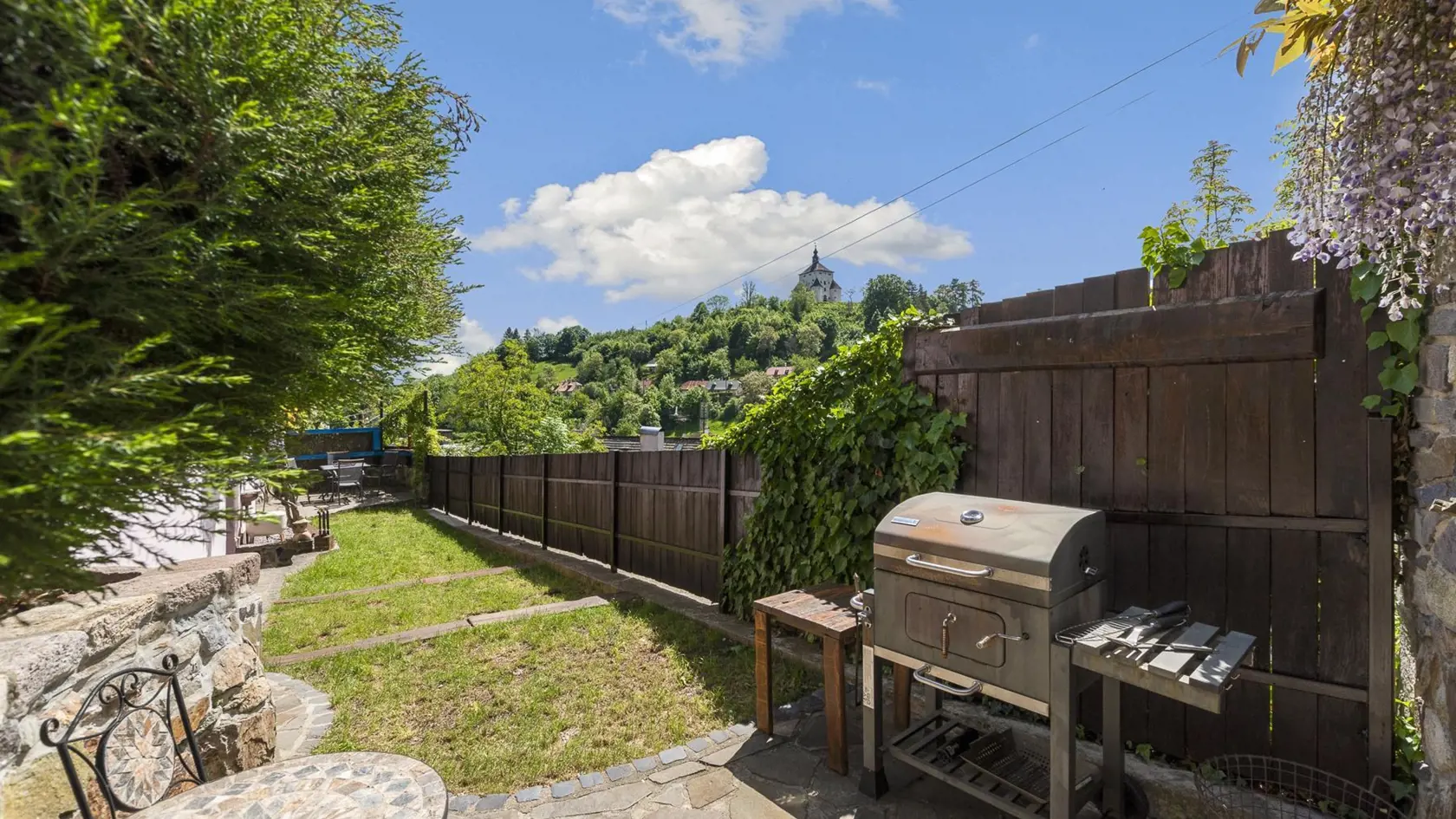 Mierne kaskádový pozemok s prekrásnou fialovo-bielou vistériou poskytuje dve veľkorysé terasy vhodné na posedenie s priateľmi a letné barbecue v malebnom prostredí historického banského mestečka.