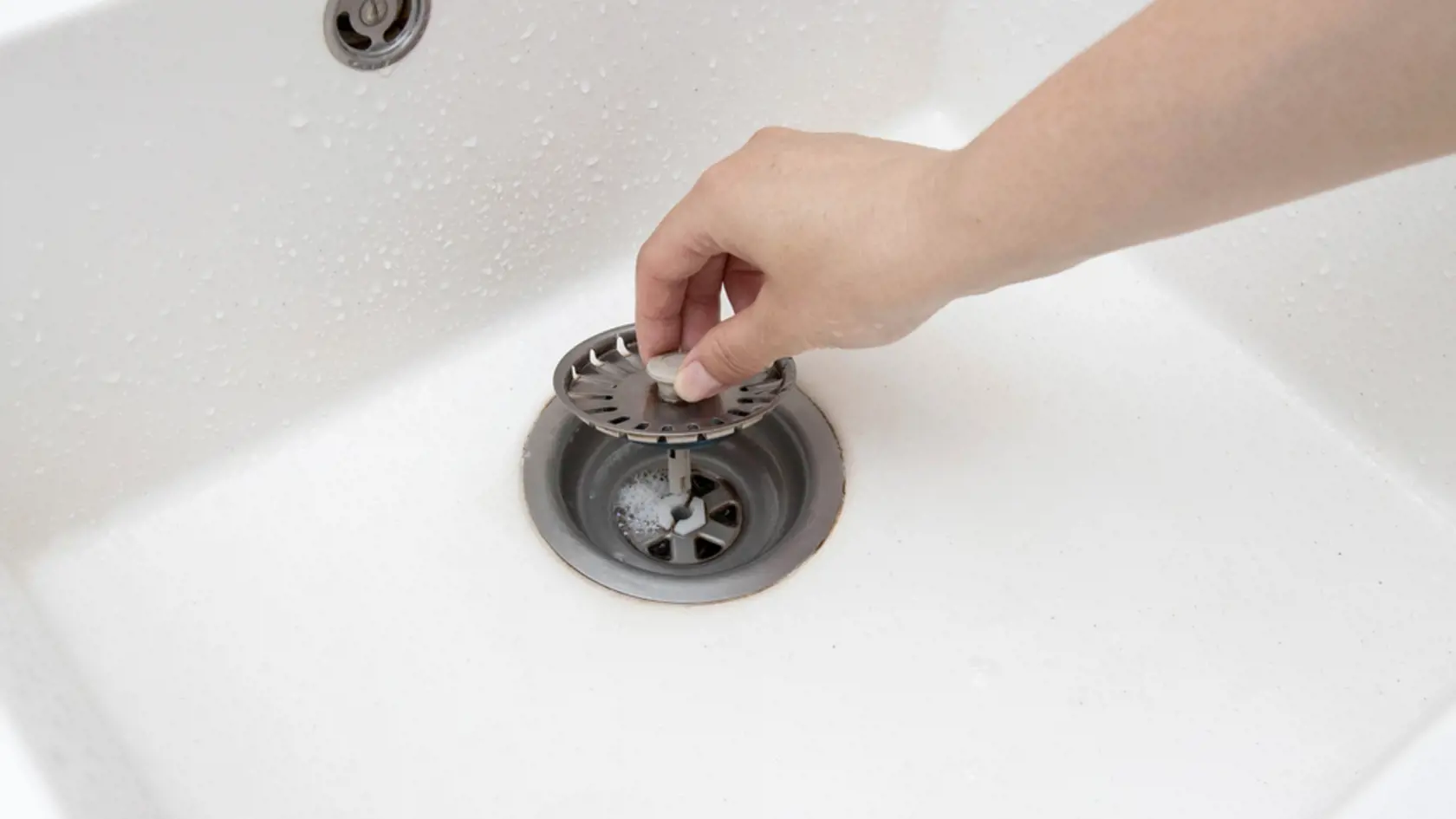 A man's hand removes a metal strainer from a kitchen sink drain. Cleaning the drain and pipes from clogging with food particles after washing dishes
