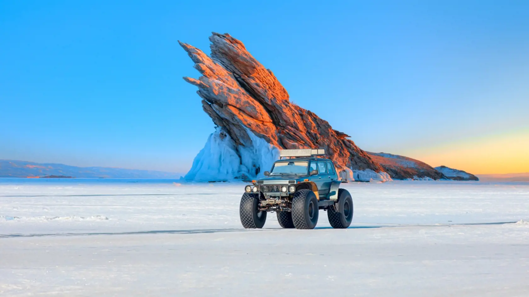 Ogoy island on winter Baikal lake with transparent cracked ice - A moving a thick-wheeled suv car on lake Baikal - Car tire tracks (trail) in fresh snow - Baikal Lake, Siberia