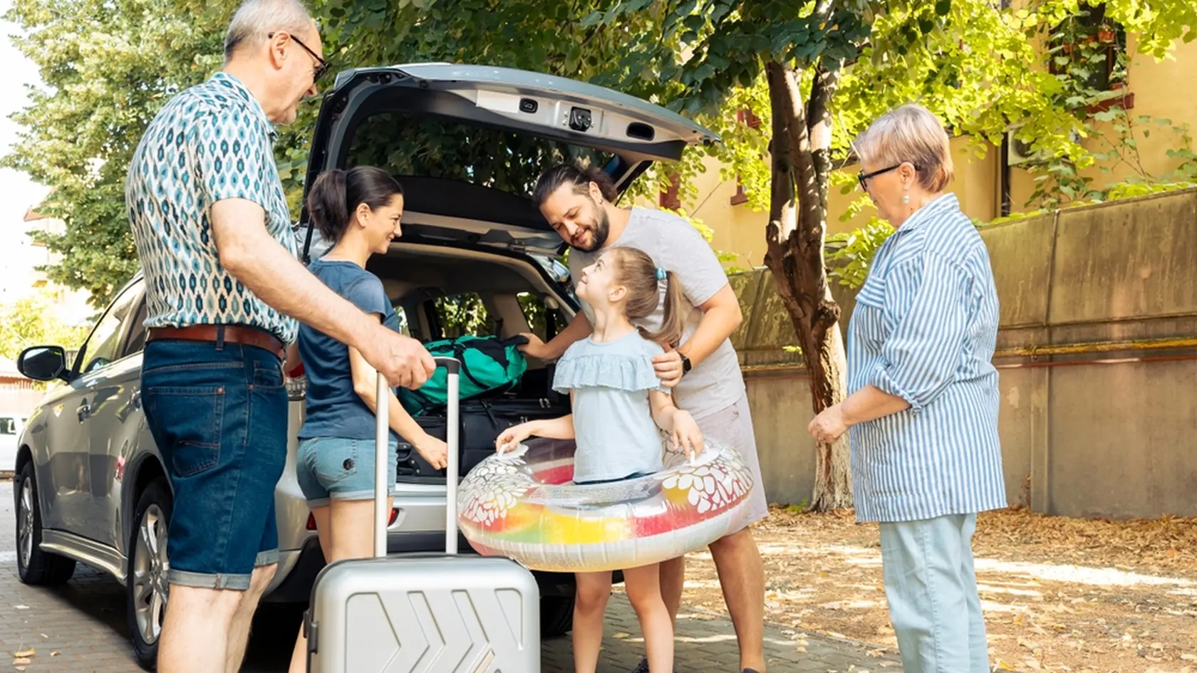 Happy family travelling at seaside with car, leaving on vacation trip with parents, grandparents and small girl. Loading luggage and suitcase in automobile trunk, summer adventure.