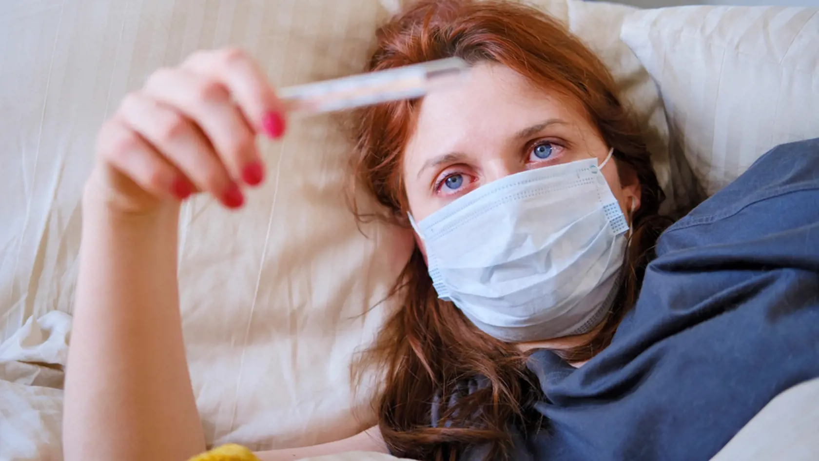 Young,Red-haired,Woman,Looks,At,A,Thermometer,While,Lying,In