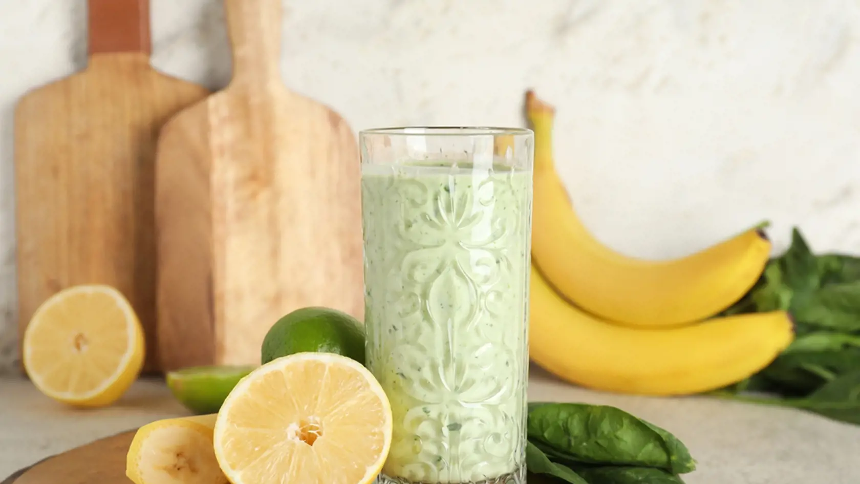 Glass of fresh spinach smoothie with lemon and banana on white background