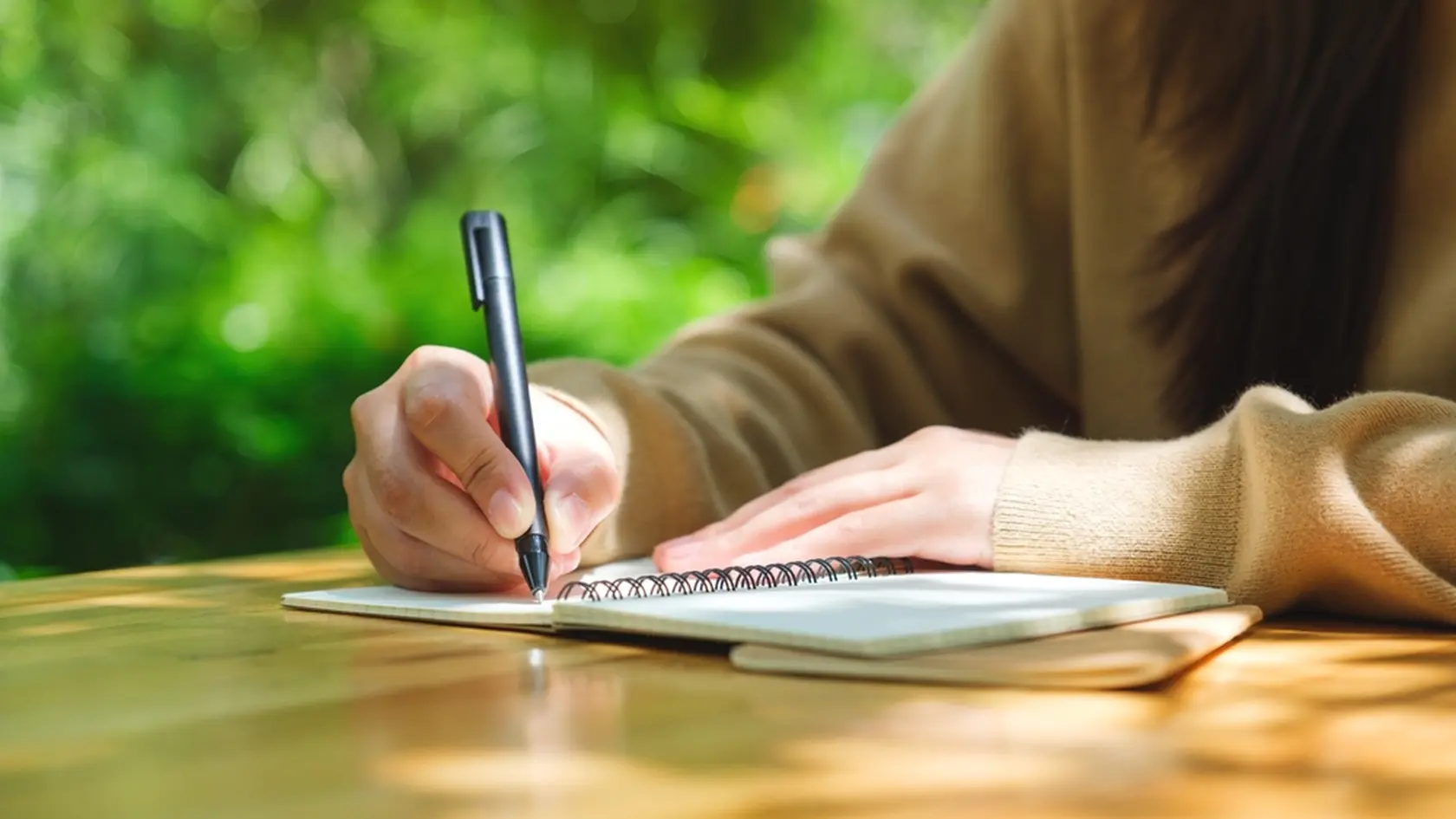 Closeup image of a woman writing on a notebook on wooden table