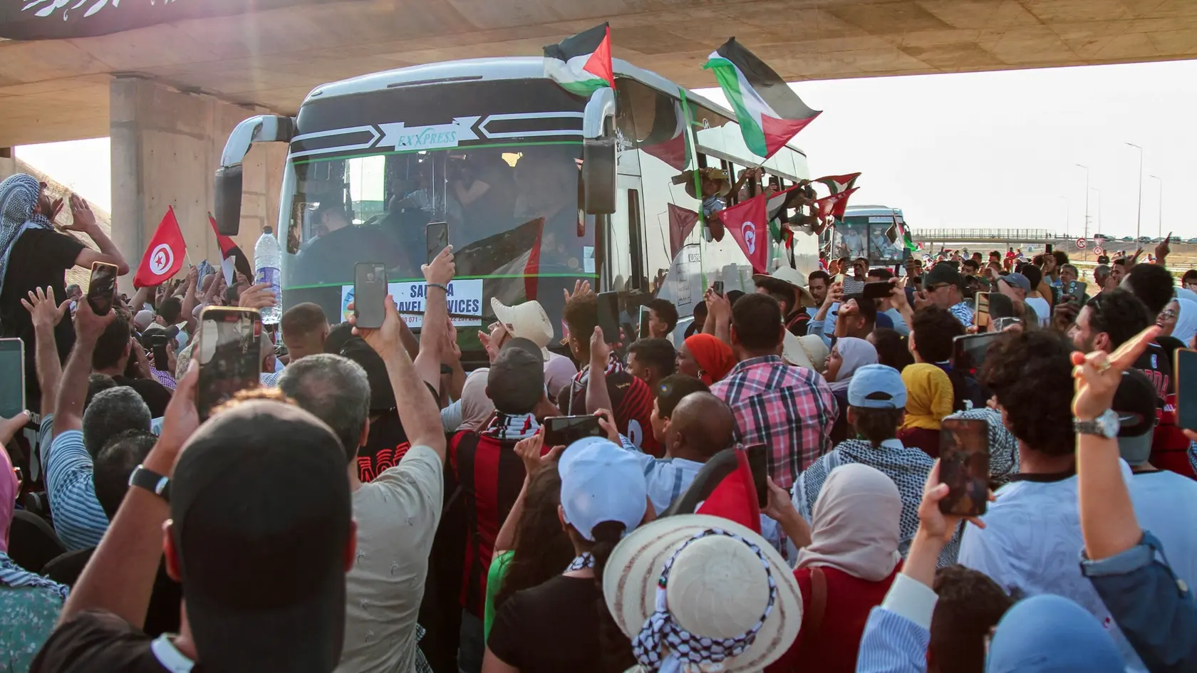 Ľudia vítajú aktivistov v autobusoch, ktorí vyrazili po súši z tuniského hlavného mesta Tunis k egyptským hraniciam s Pásmom Gazy, aby tak prejavili solidaritu s obyvateľmi tejto palestínskej enklávy v tuniskom meste Gábes v pondelok 9. júna 2025.