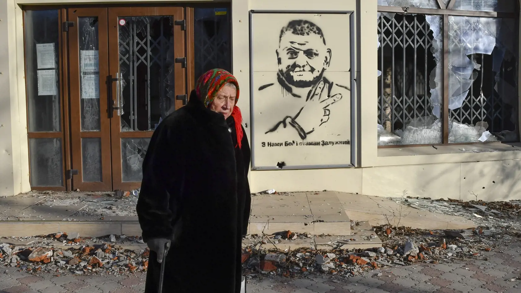 Staršia žena kráča po ulici v oblasti ťažkých bojov s ruskými silami v meste Bachmut, na východe Ukrajiny 20. decembra 2022. V pozadí graffiti s portrétom generála Valerija Zalužného, veliteľa ukrajinských ozbrojených síl.
