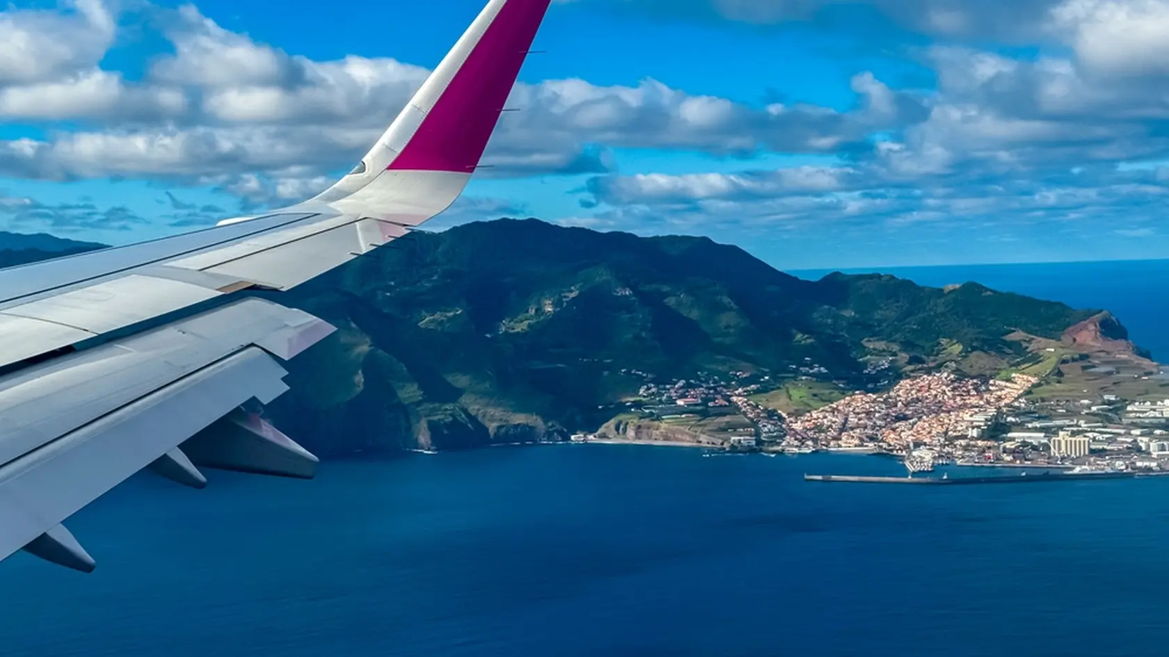 Aerial window view from an airplane on coastal town Canical, Madeira Islands, Portugal, Europe. Wing and turbines of the aircraft. Flying high above ground. Freedom. Flying into vacation