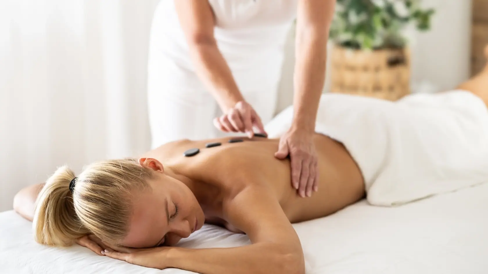 Beatiful woman is enjoying relaxing back massage in cosmetology spa centre. The masseuse applies lava stones to the spine.