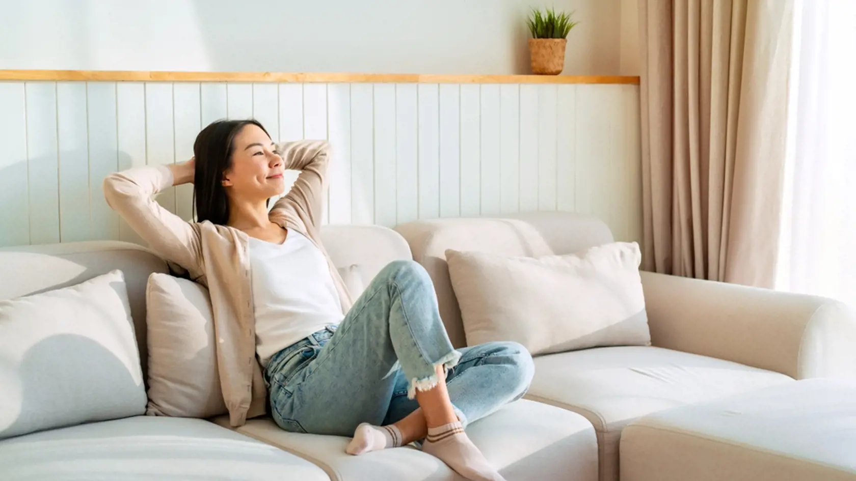 Carefree Asian woman relaxing and sitting on a sofa at home in the morning