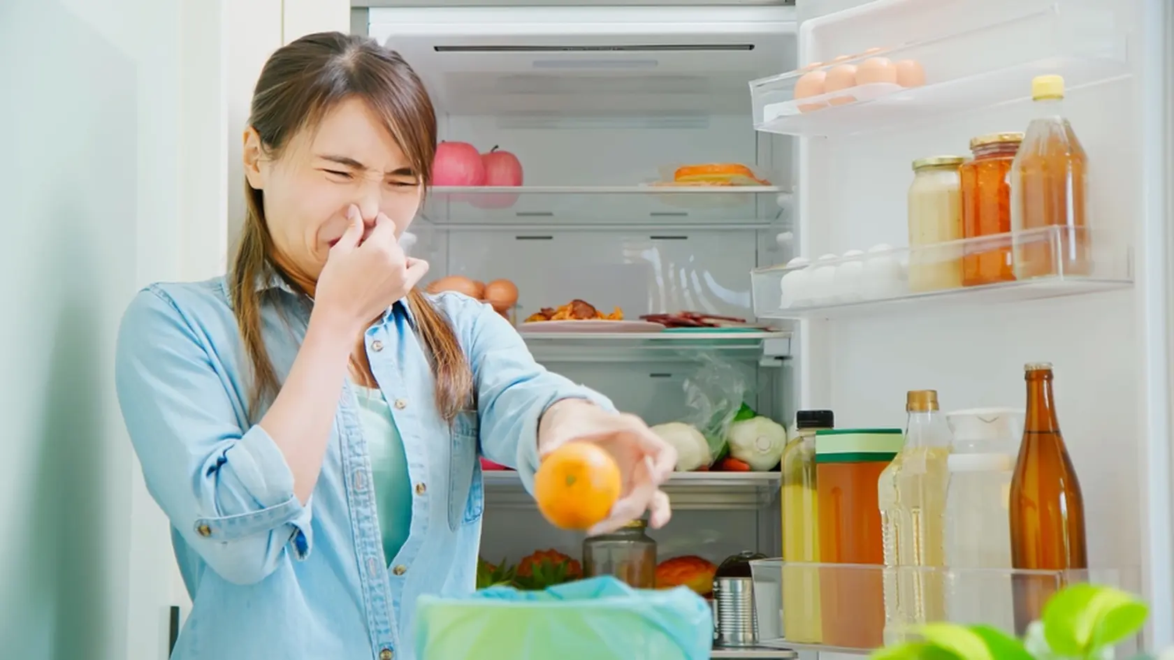 asian woman is cleaning refrigerator and pouring food waste which smell bad into kitchen bucket at home