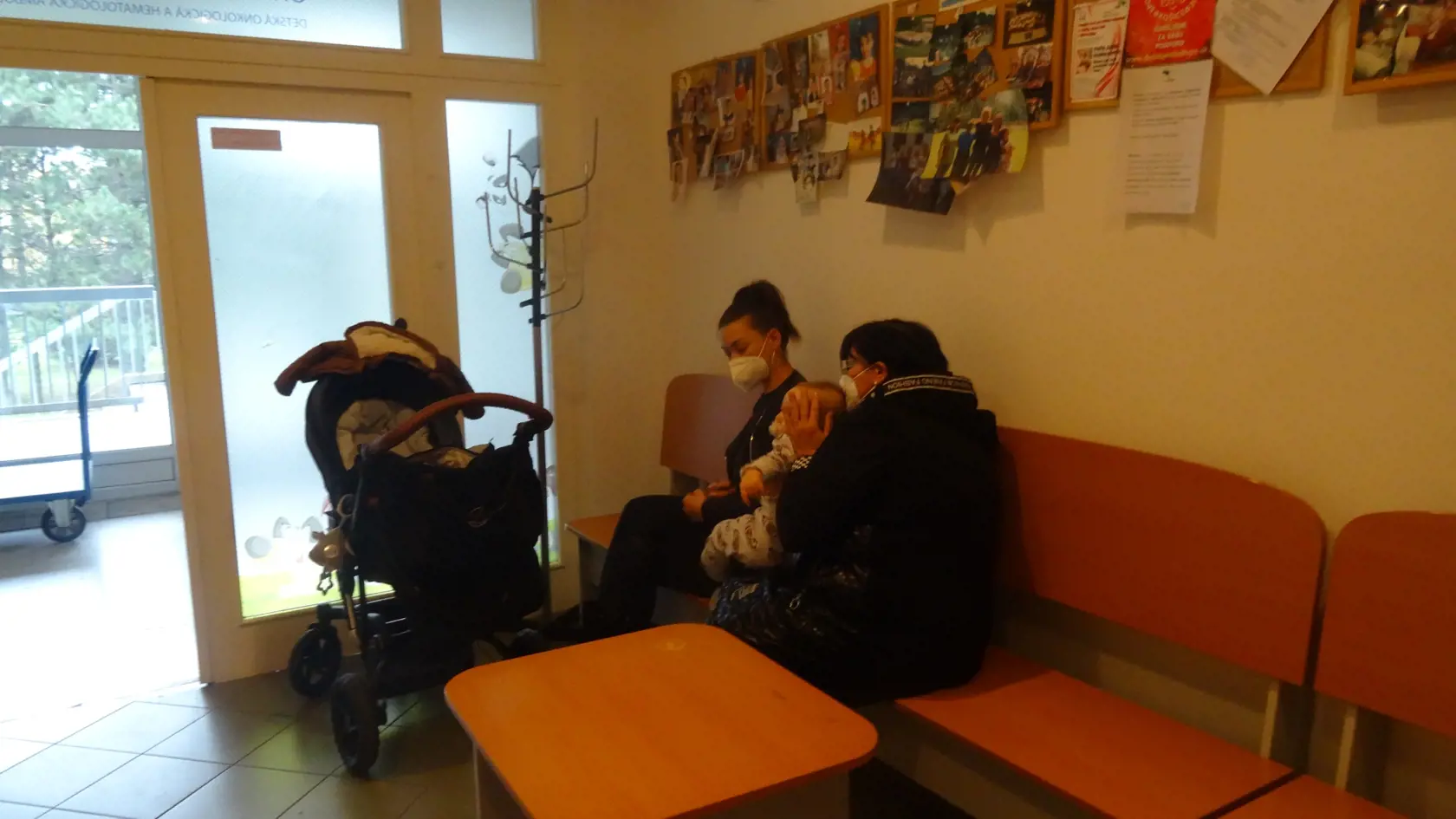 Babka s dcérou a vnúčaťom v malej čakárni. Priestor zvyknú vetrať cez otvorené dvere, keďže okno tam chýba.