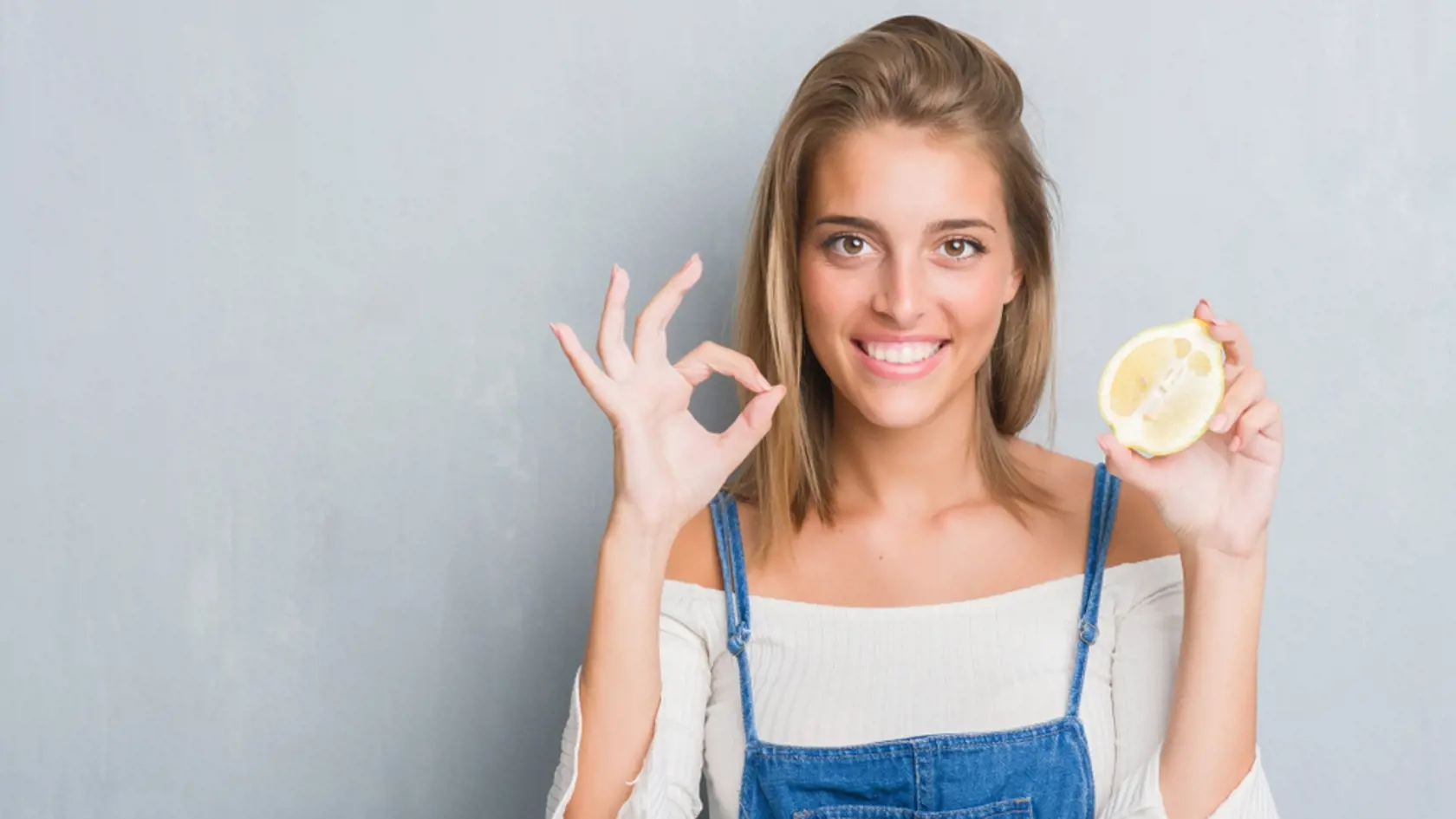 Beautiful,Young,Woman,Over,Grunge,Grey,Wall,Holding,A,Lemon