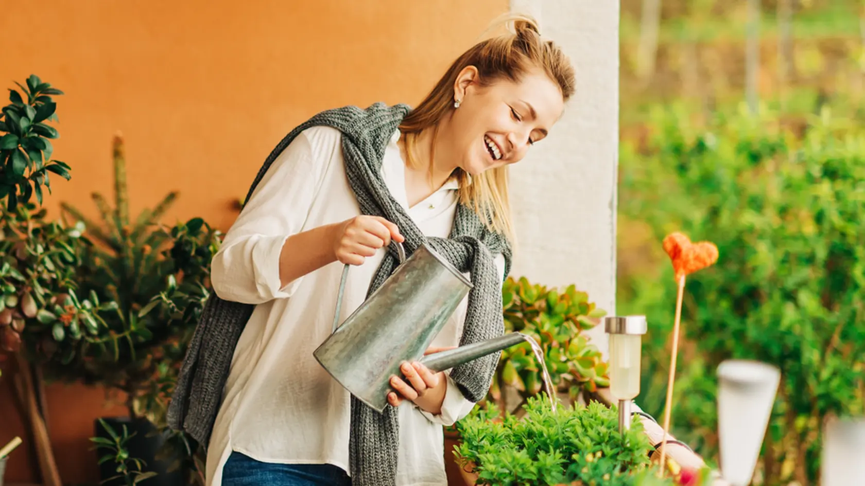 Portrait of beautiful woman watering green plants on the balcony, small cozy garden in apartment