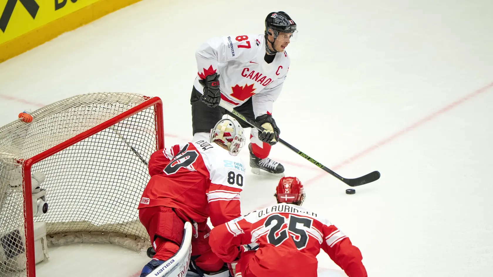 Kapitán Kanady Sidney Crosby (v pozadí), brankár Dánska Frederik Dichow (uprostred) a hokejista Dánska Oliver Lauridse