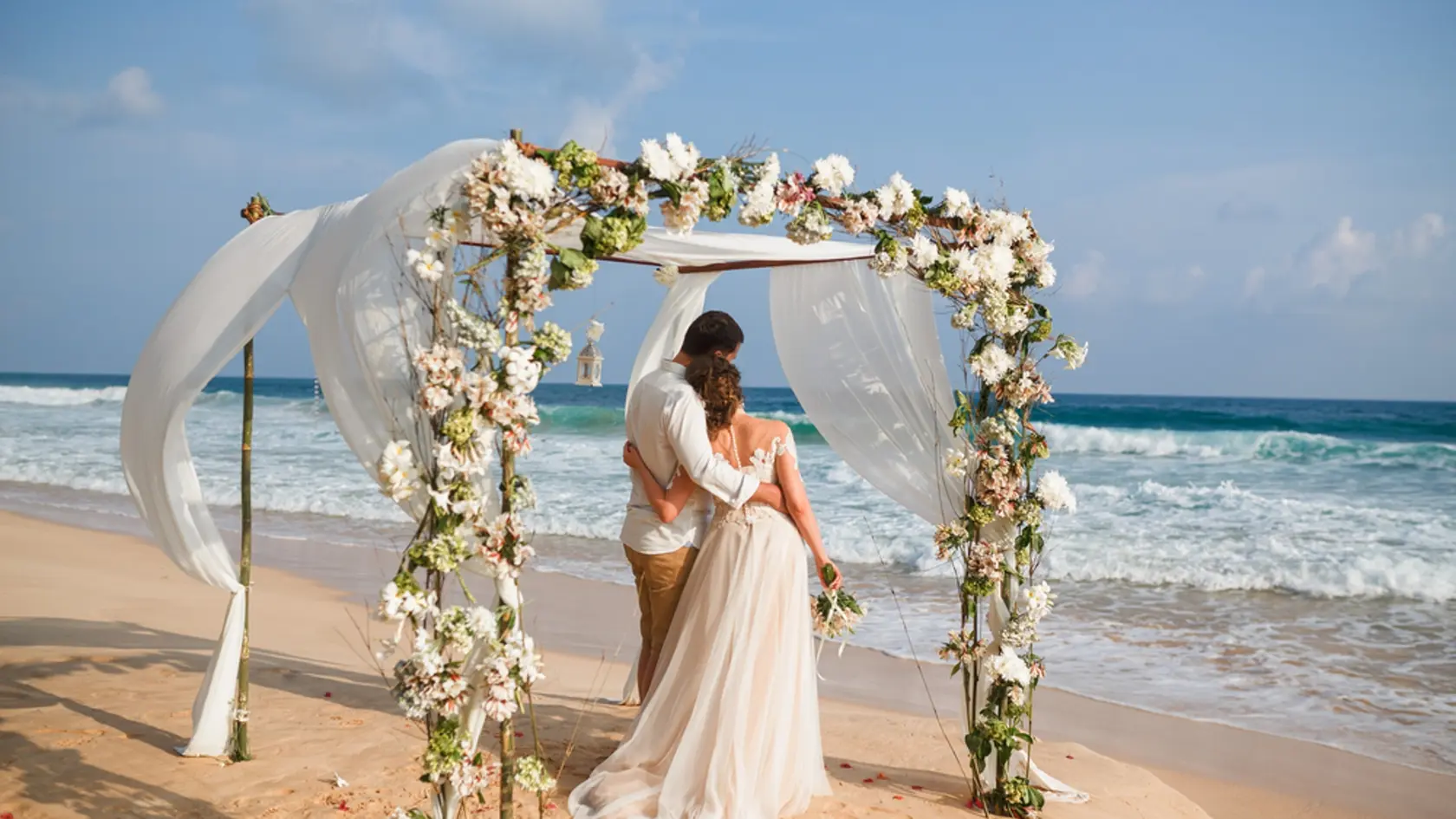 Bride and groom enjoying beach wedding in tropics,  wedding arch, ocean background