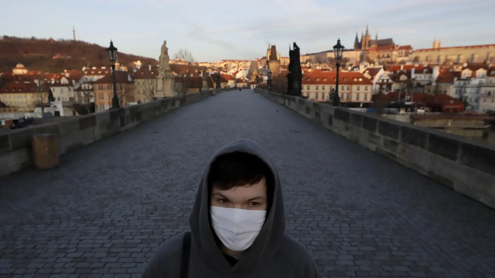 Mladý muž s ochranným rúškom na tvári kráča po Karlovom moste.