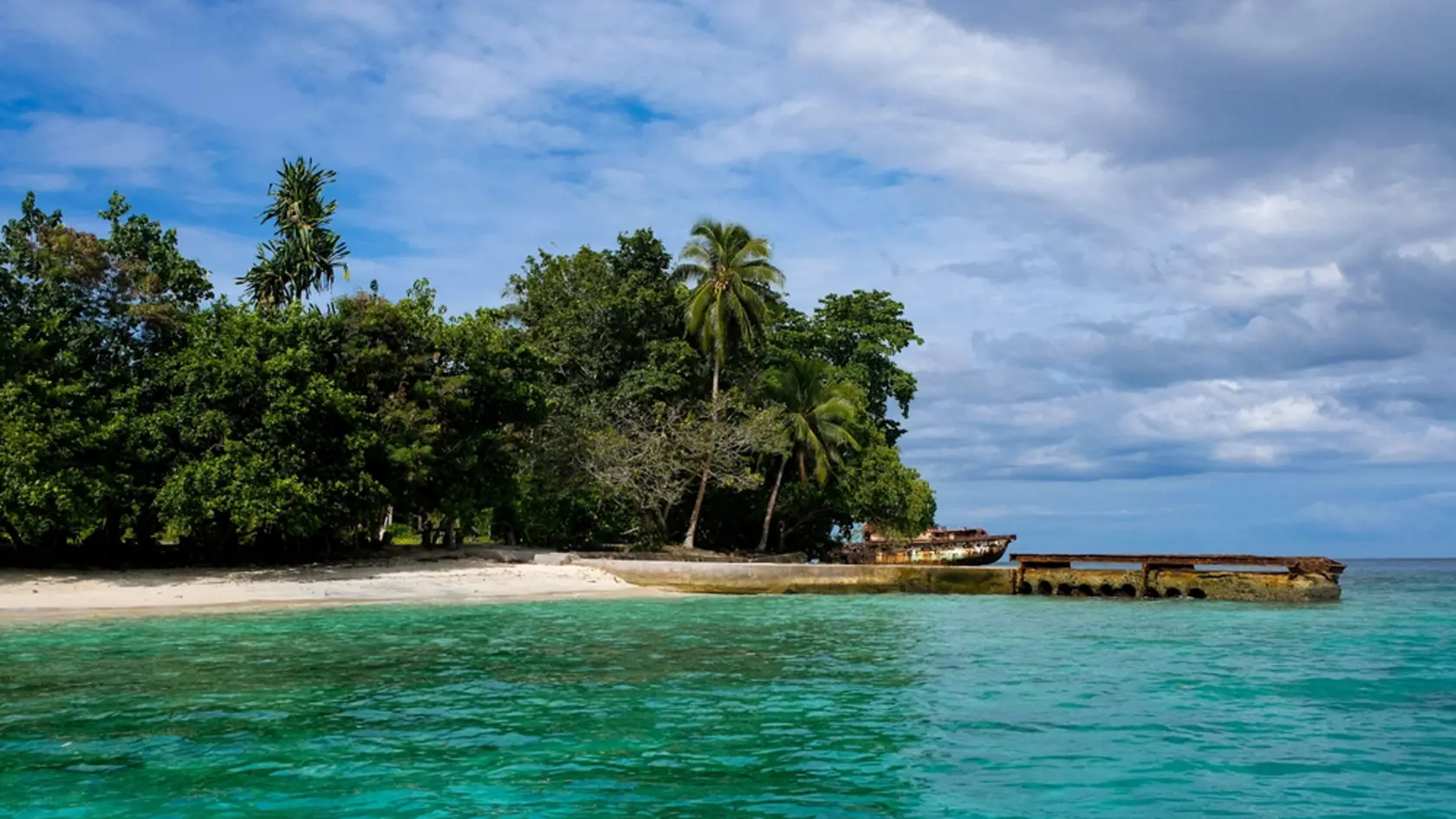 Scenic idyllic view of a remote tropical island covered in trees with an old jetty wharf and stunning turquoise ocean water in Bougainville, Papua New Guinea