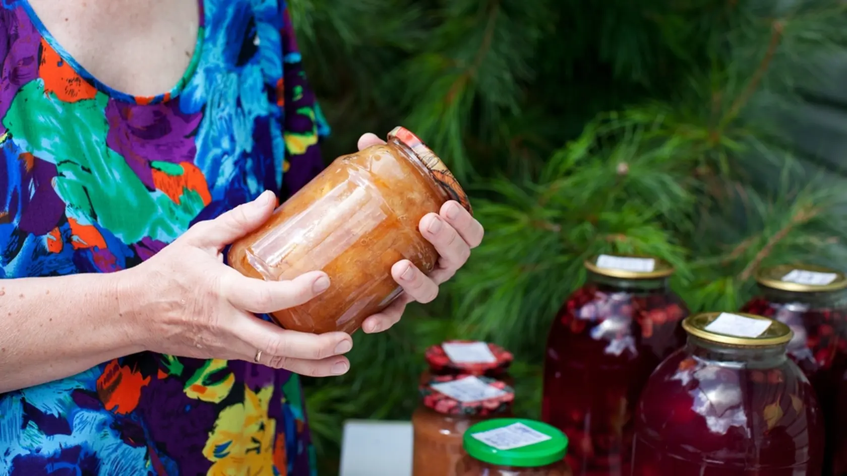 Elderly woman holds jar of homemade conserved jam in her hands