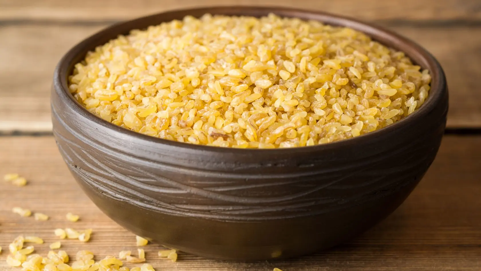 Dry bulgur wheat in ceramic bowl on rustic wooden background. Selective focus.