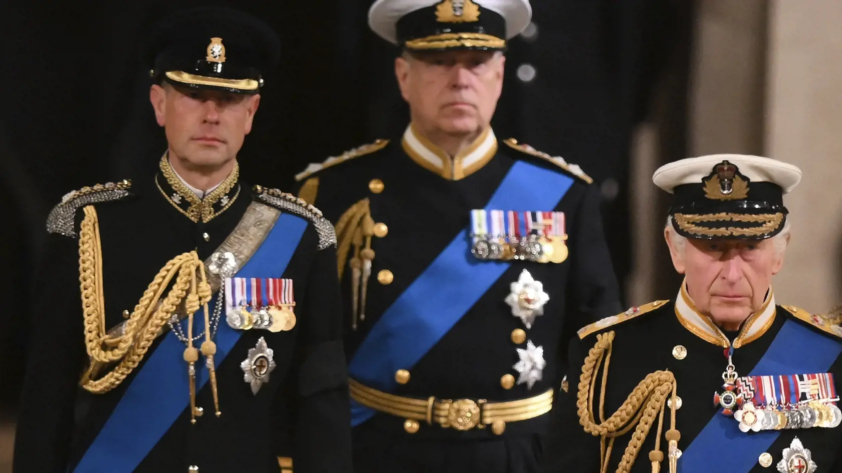 Všetci traja synovia zosnulej britskej kráľovnej Alžbety II. - sprava britský kráľ Karol III., princovia  Andrew a Edward oblečení v slávnostných uniformách - prichádzajú na večernú vigíliu do Westminsterskej sály v Londýne v piatok 16. septembra 2022. Dvere Westminsterskej sály zatvoria v pondelok ráno o 06.30 h miestneho času (07.30 h SELČ). O štyri hodiny neskôr prepravia rakvu na delovej lafete v sprievode členov kráľovskej rodiny do Westminsterského opátstva.