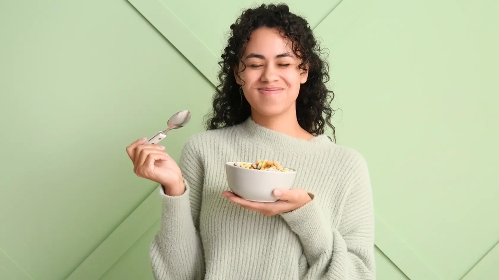 Emotional woman eating tasty cereal rings against color wall