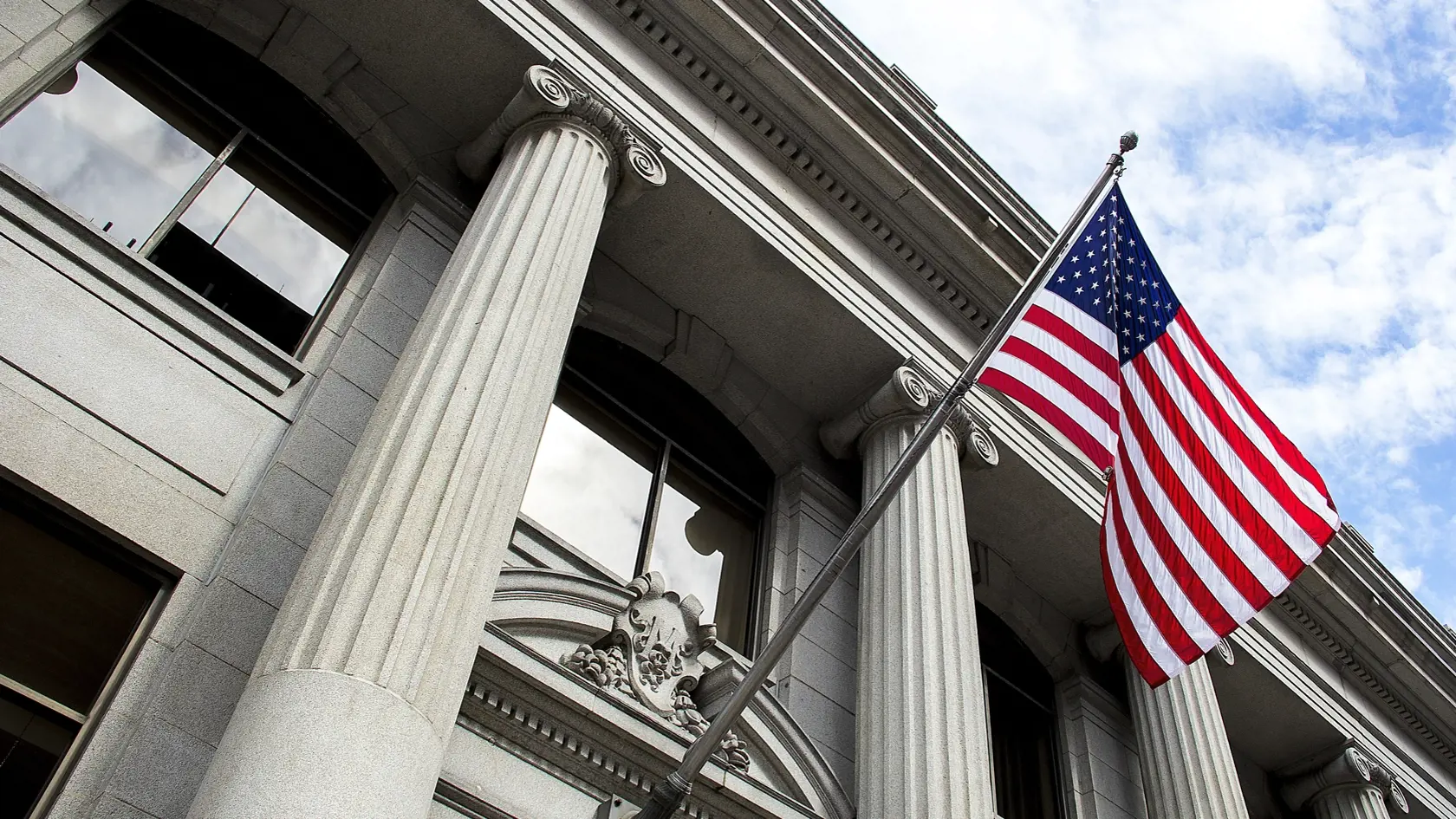 Stone granite official government building in city with American flag waving and flying in the wind, looking up, outside, judicial, freedom, civil courts, columns, criminal justice, law