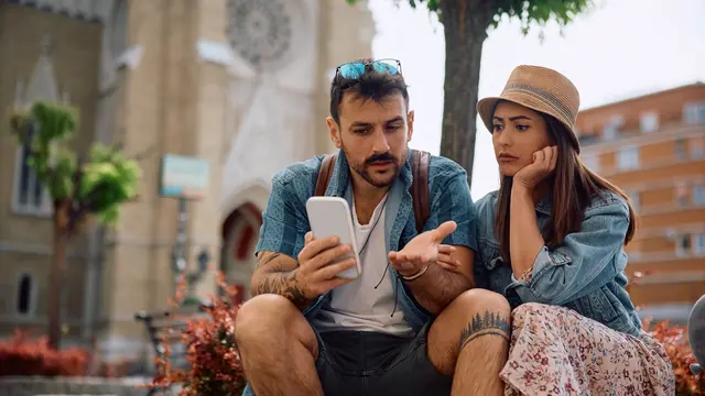 Distraught couple of tourists using app on mobile phone while exploring the city. 