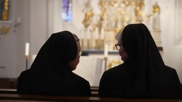 Warstein, Germany, 05.19.2024: Two Christian Nuns, Seen From Behind, Sitting In The Church And Looking To Each Other. Traditional Black Clothes. 